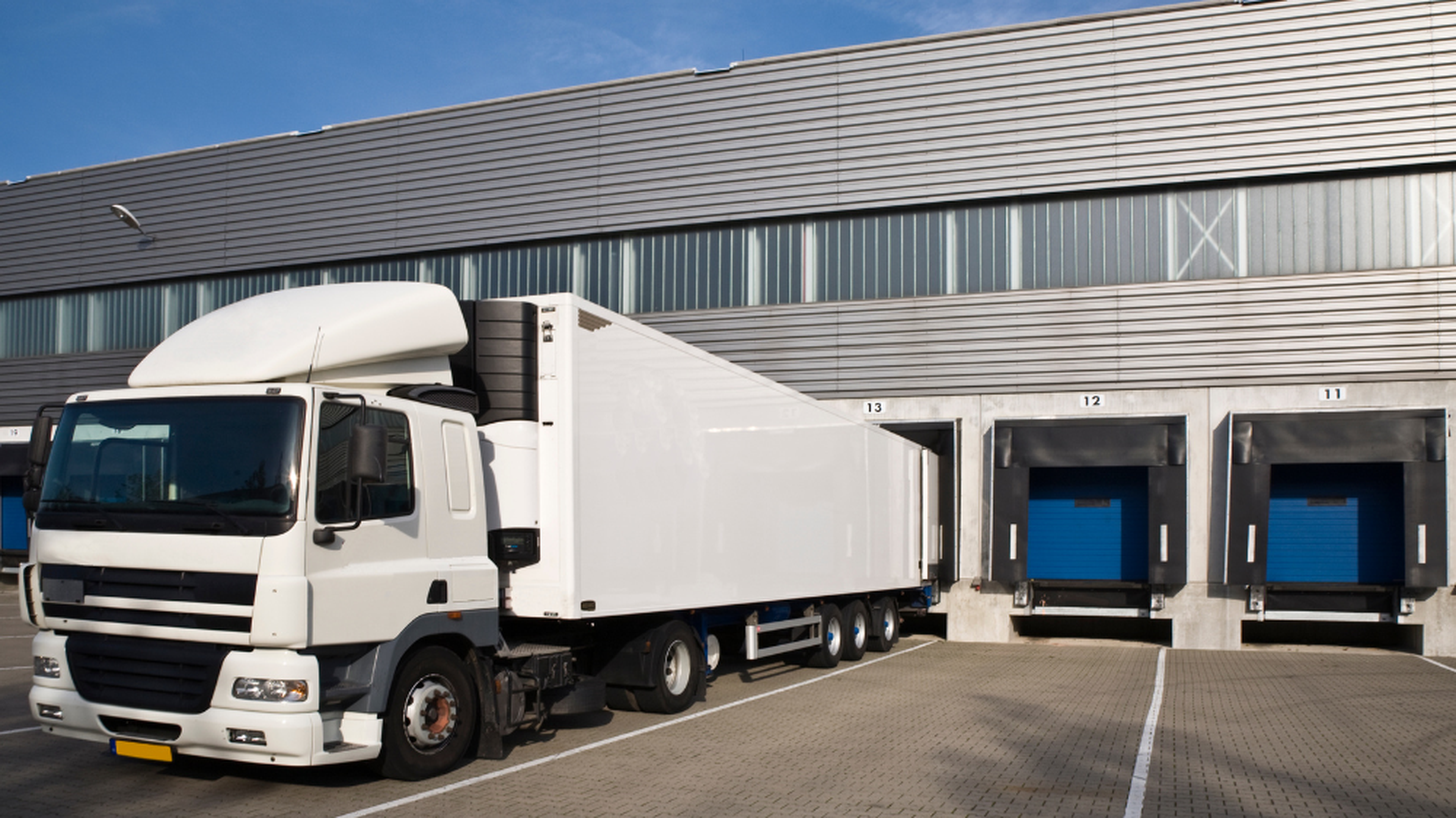 Camion blanc stationné à un quai de chargement d’un entrepôt industriel, avec plusieurs quais identifiés, illustrant la visibilité transport et la gestion des livraisons à quai.