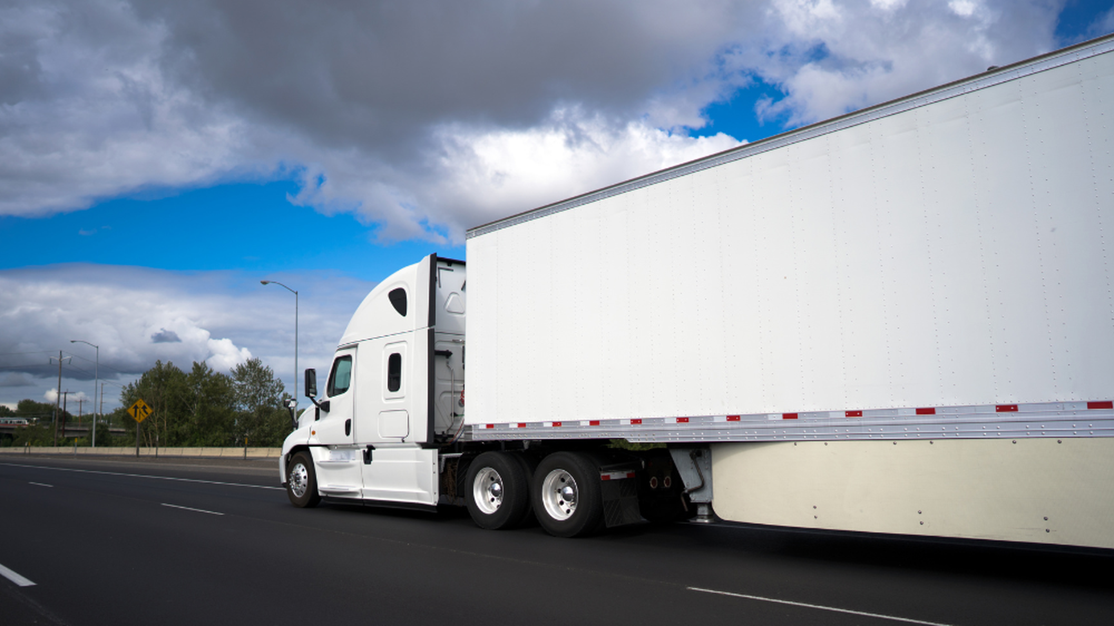 Camion semi-remorque blanc circulant sur l’autoroute sous un ciel nuageux, utilisé pour le transport produit frais et les tournées sous température dirigée.