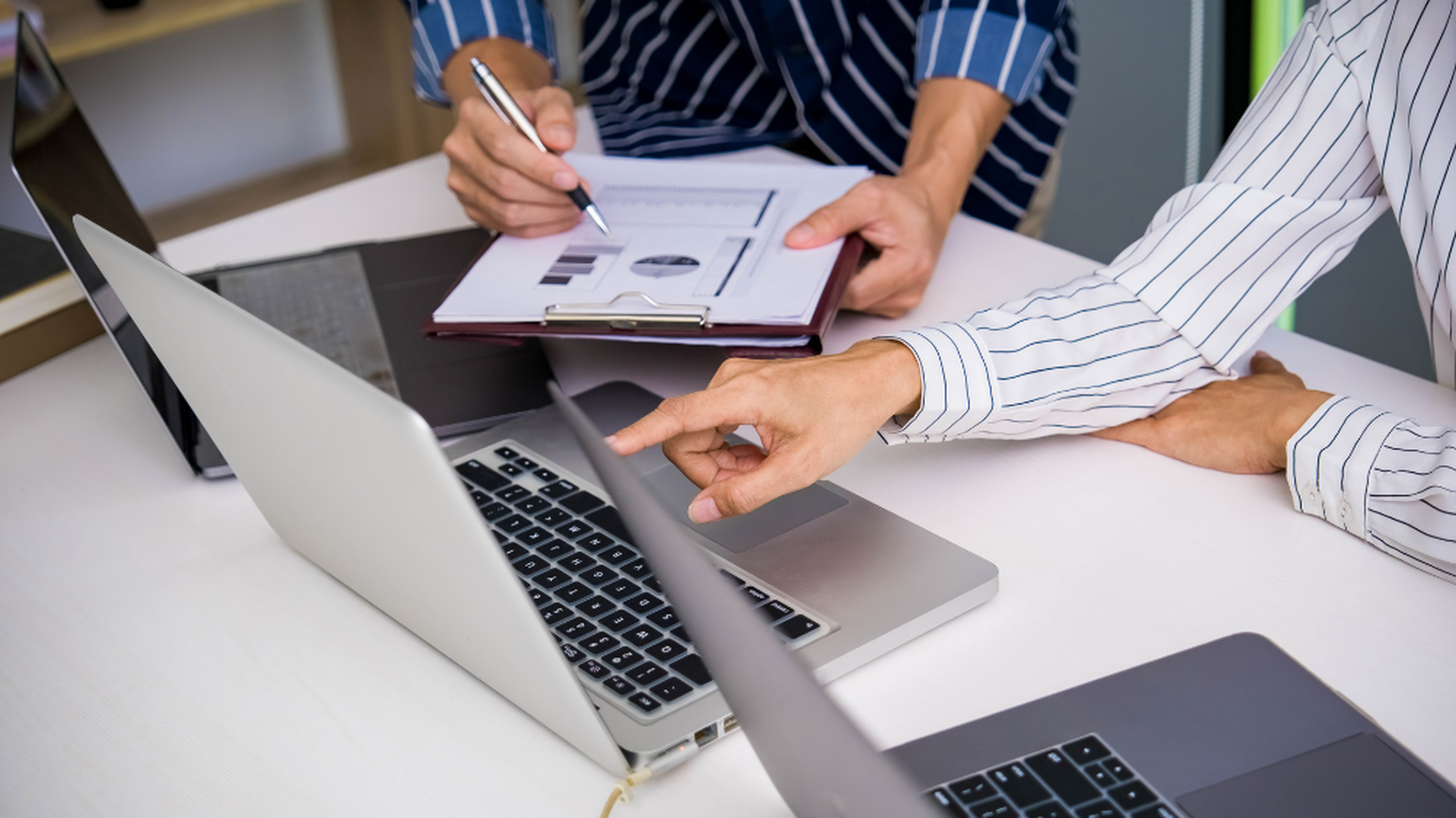 Deux personnes en chemises à rayures analysent des données sur un ordinateur portable et un clipboard, illustrant l’évaluation du ROI TMS transport.