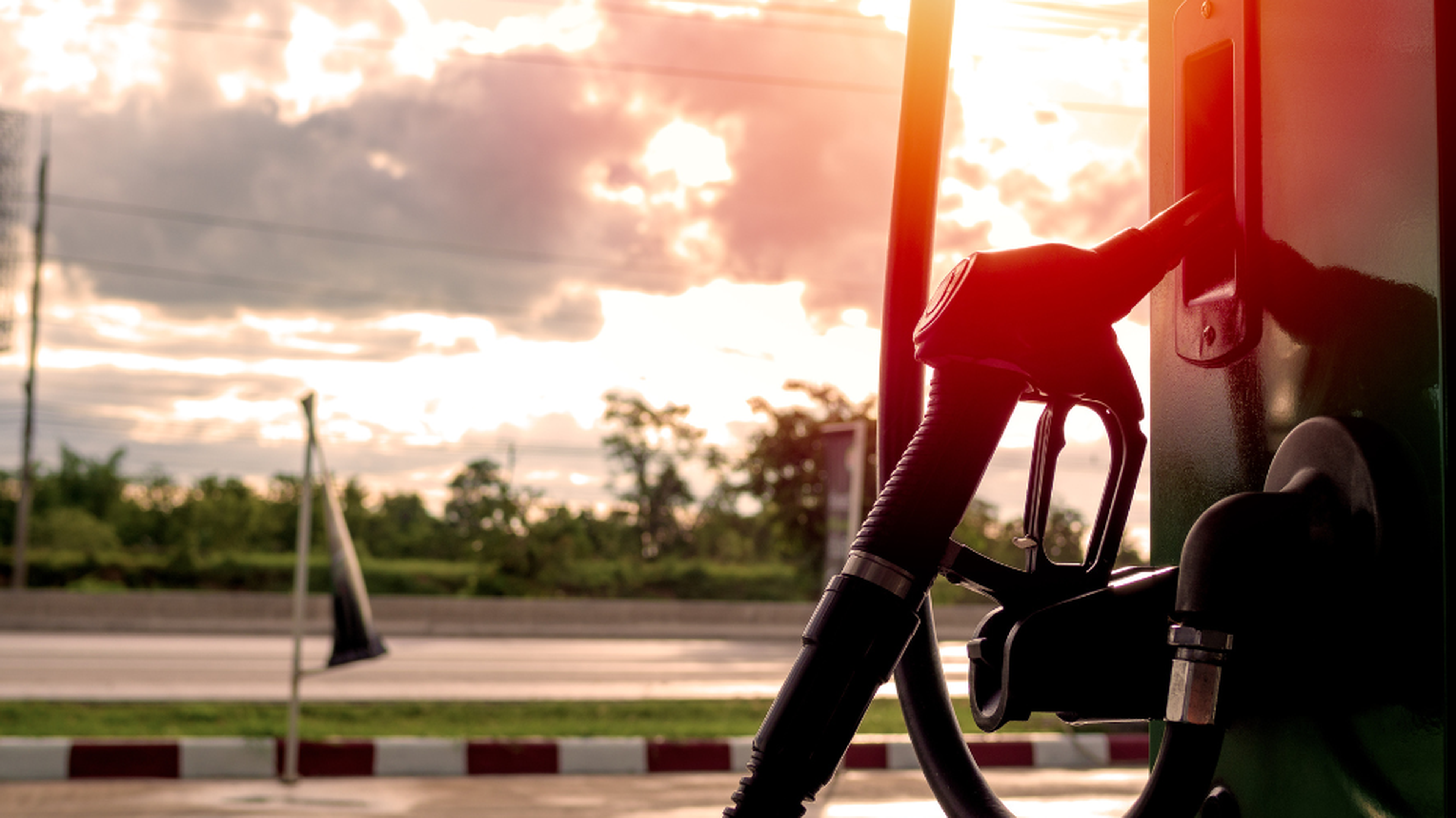 Pistolet de pompe à carburant au coucher du soleil, avec une route en arrière-plan — illustration du prix des biocarburants et de leur évolution sur le marché.