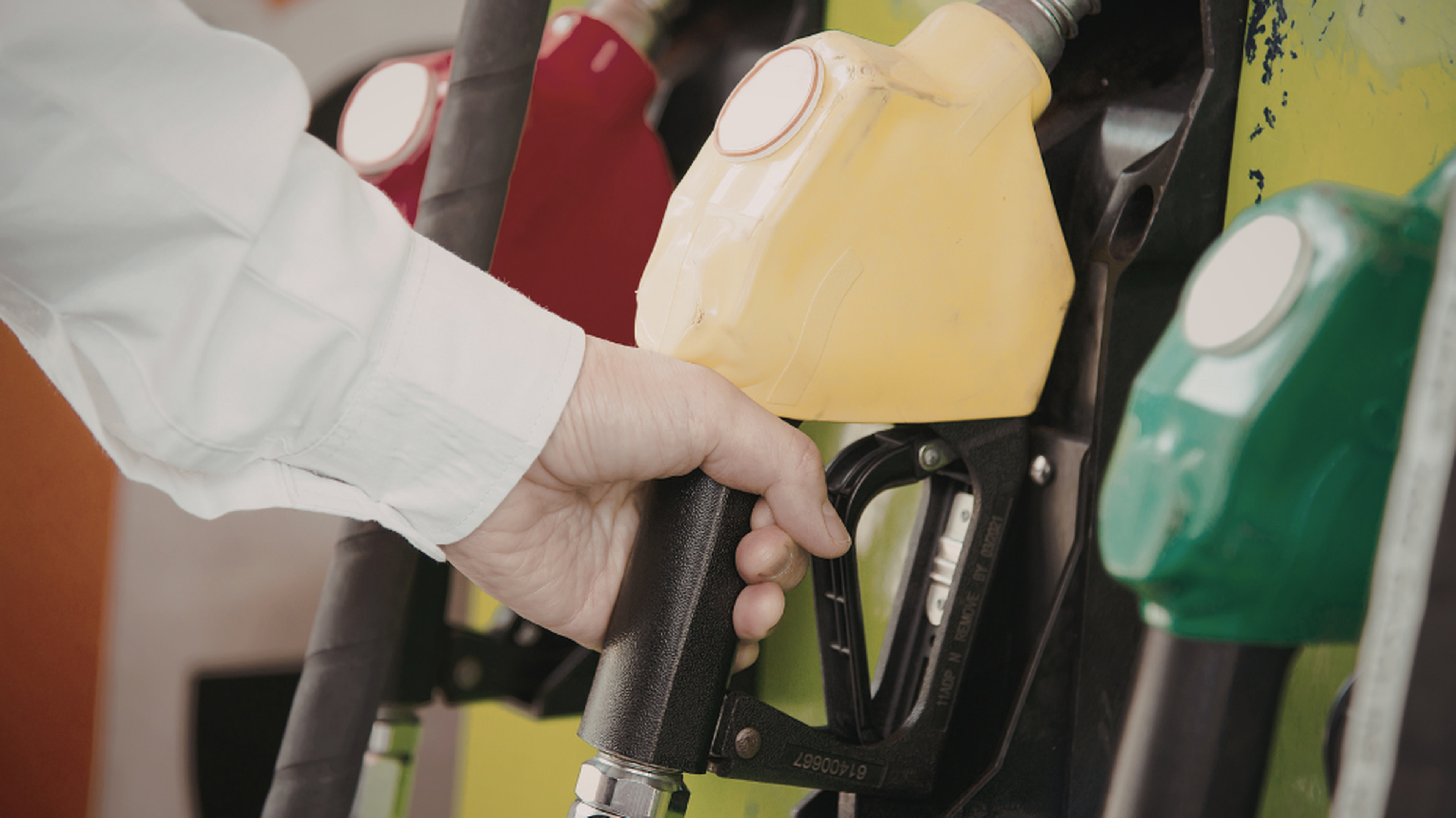 Conducteur sélectionnant un pistolet de gazole noir à la pompe, parmi des pistolets rouge, jaune et vert, illustrant le poids du carburant dans le prix du transport routier au km.