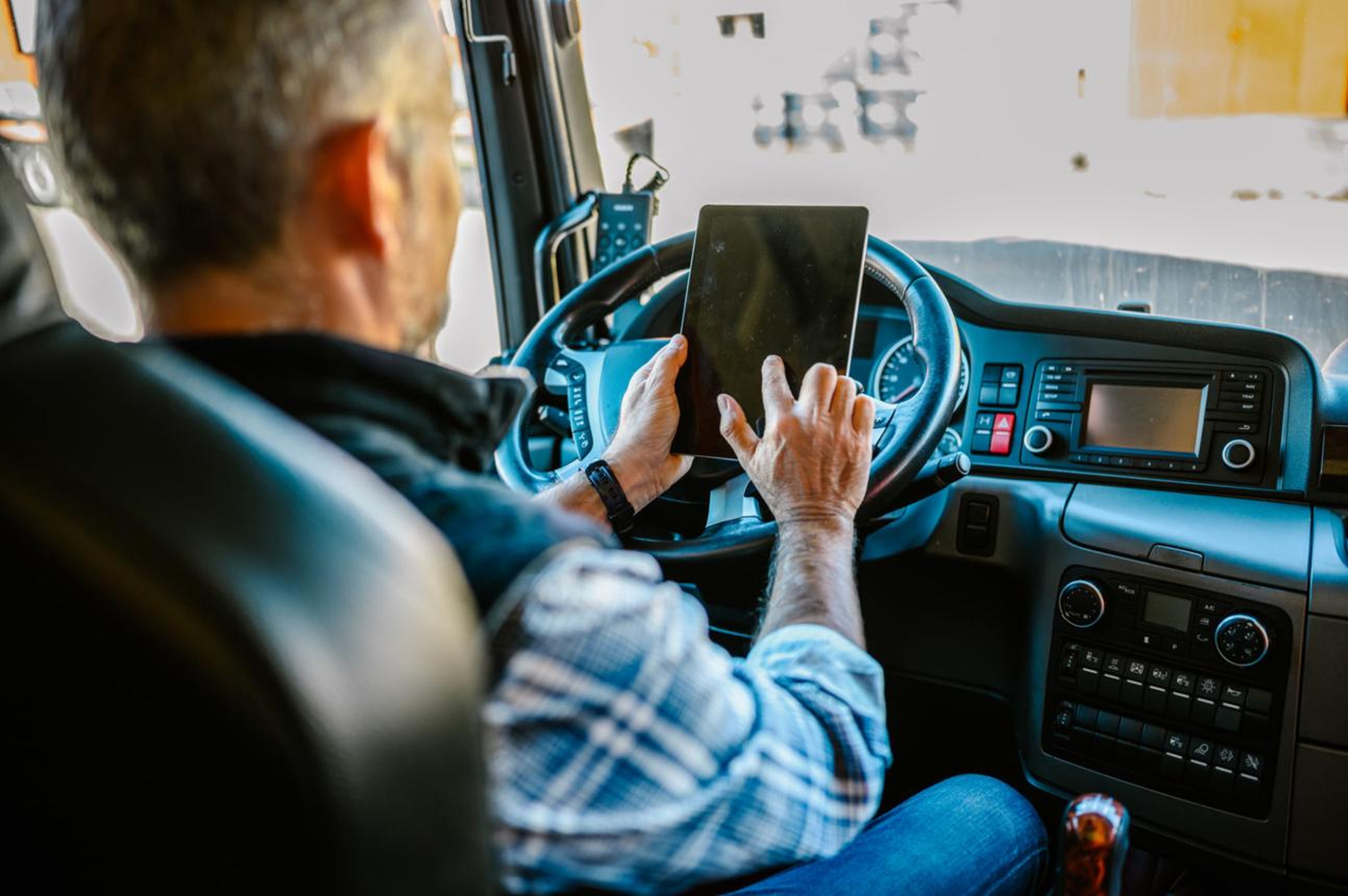 Conductor dentro de la cabina de un camión utiliza una tableta apoyada en el volante, interactuando con el documento de control digital a través de un panel de control tecnológico integrado en el vehículo.
