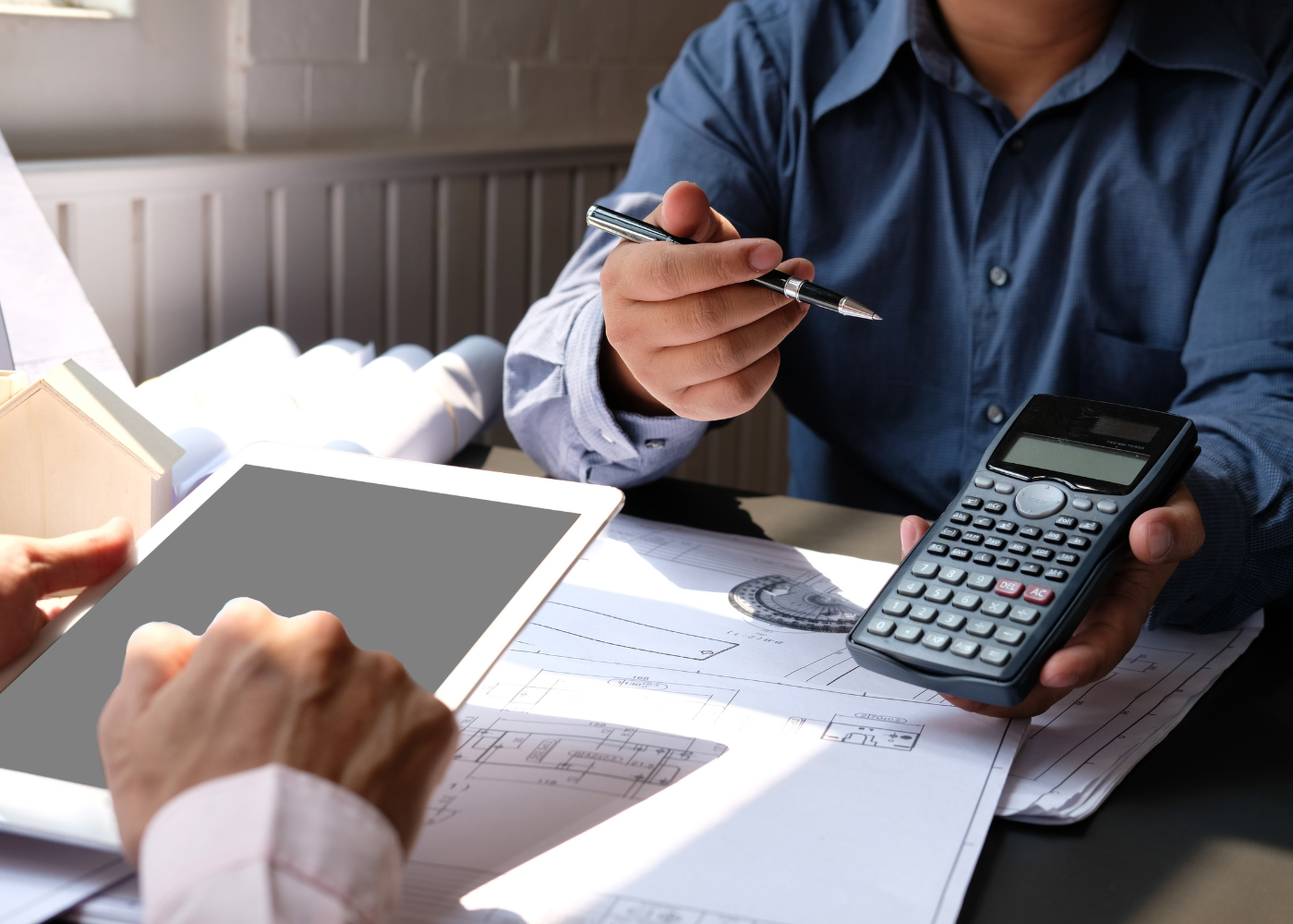 Dos personas trabajando en una mesa con una tablet, una calculadora y planos, revisando procesos de factura electrónica obligatoria.