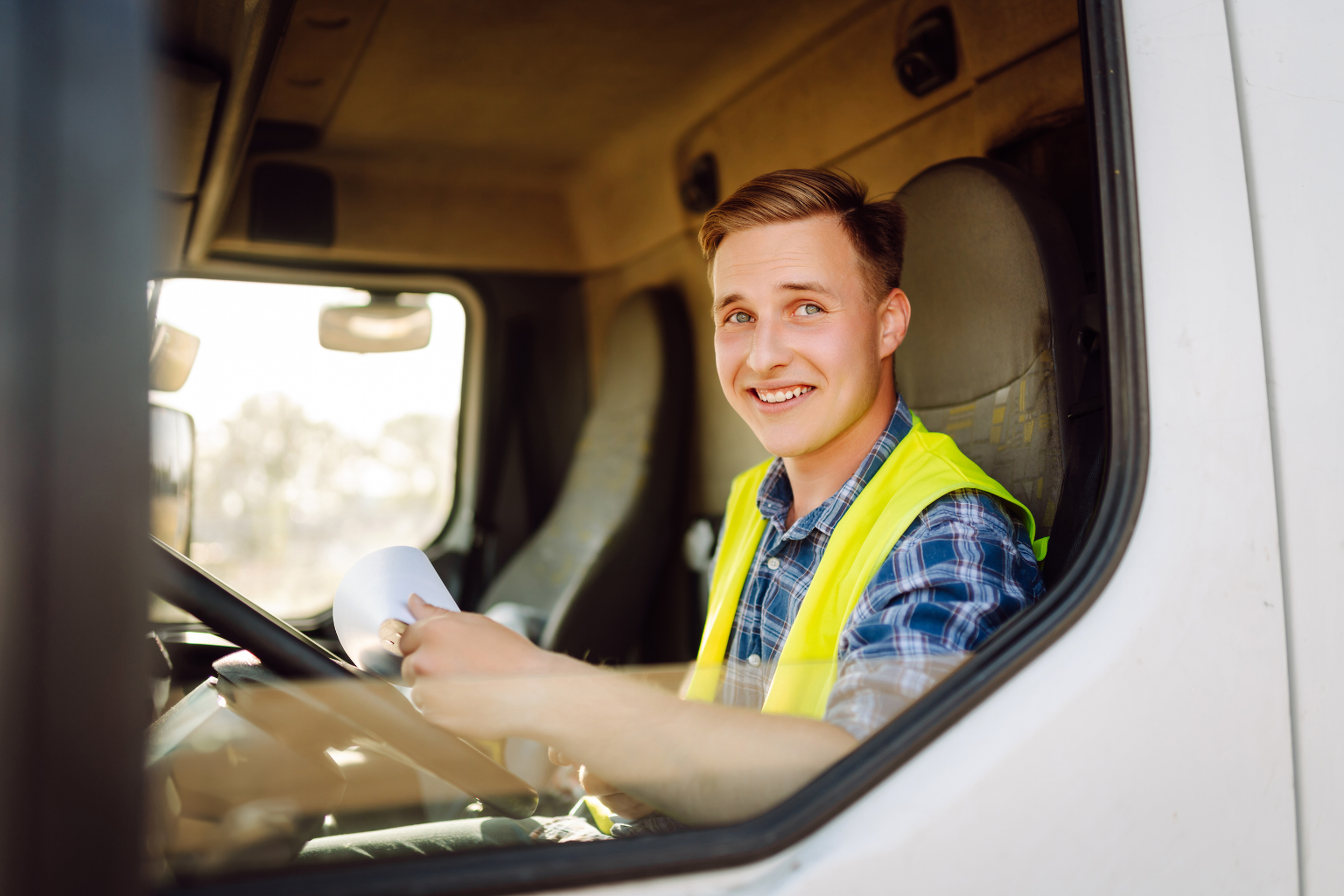 Conducteur routier souriant en gilet haute visibilité tenant des documents dans la cabine de son camion, illustrant les aides au transport routier et la gestion administrative des dossiers
