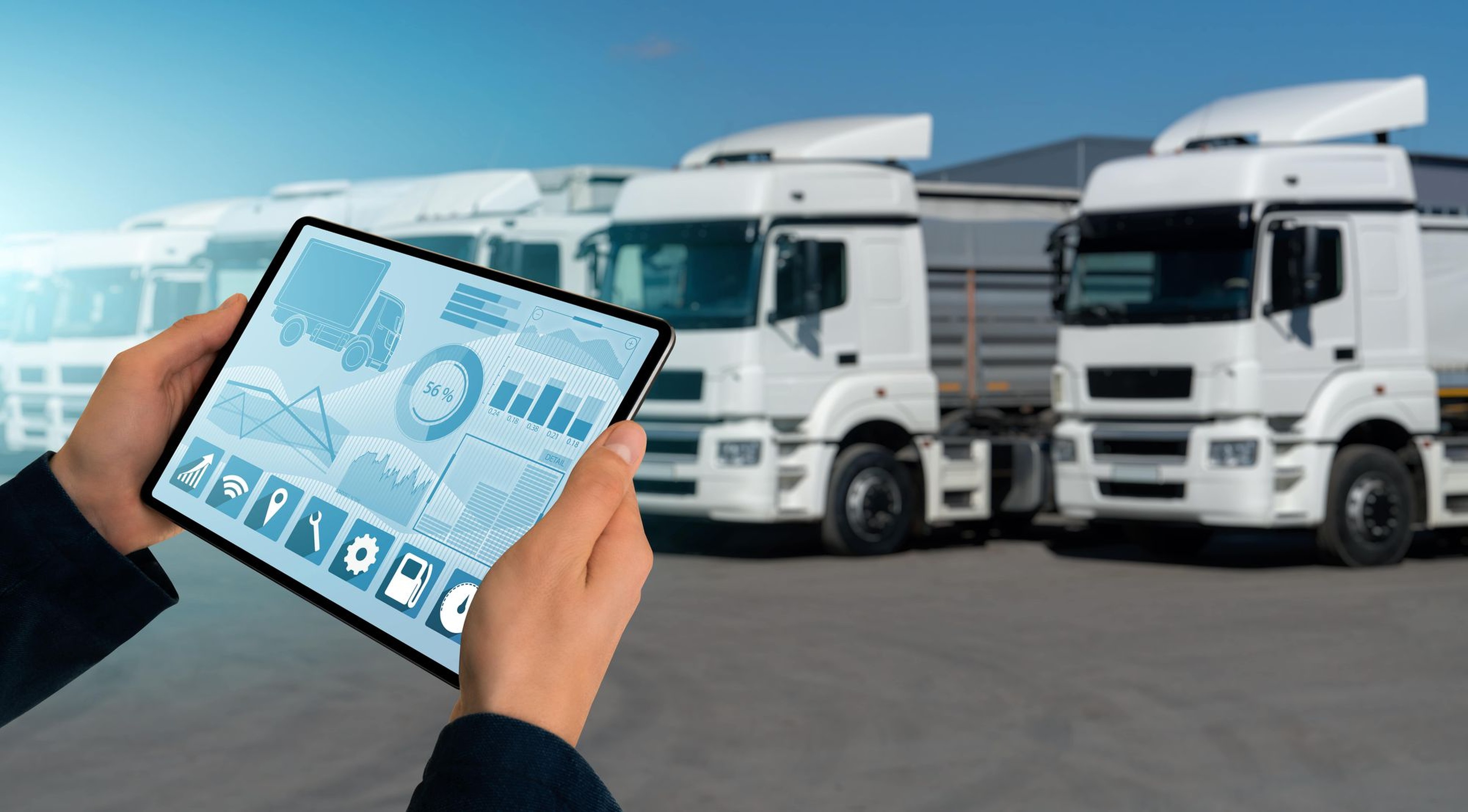 Homme avec une tablette dans les mains devant une flotte de camion