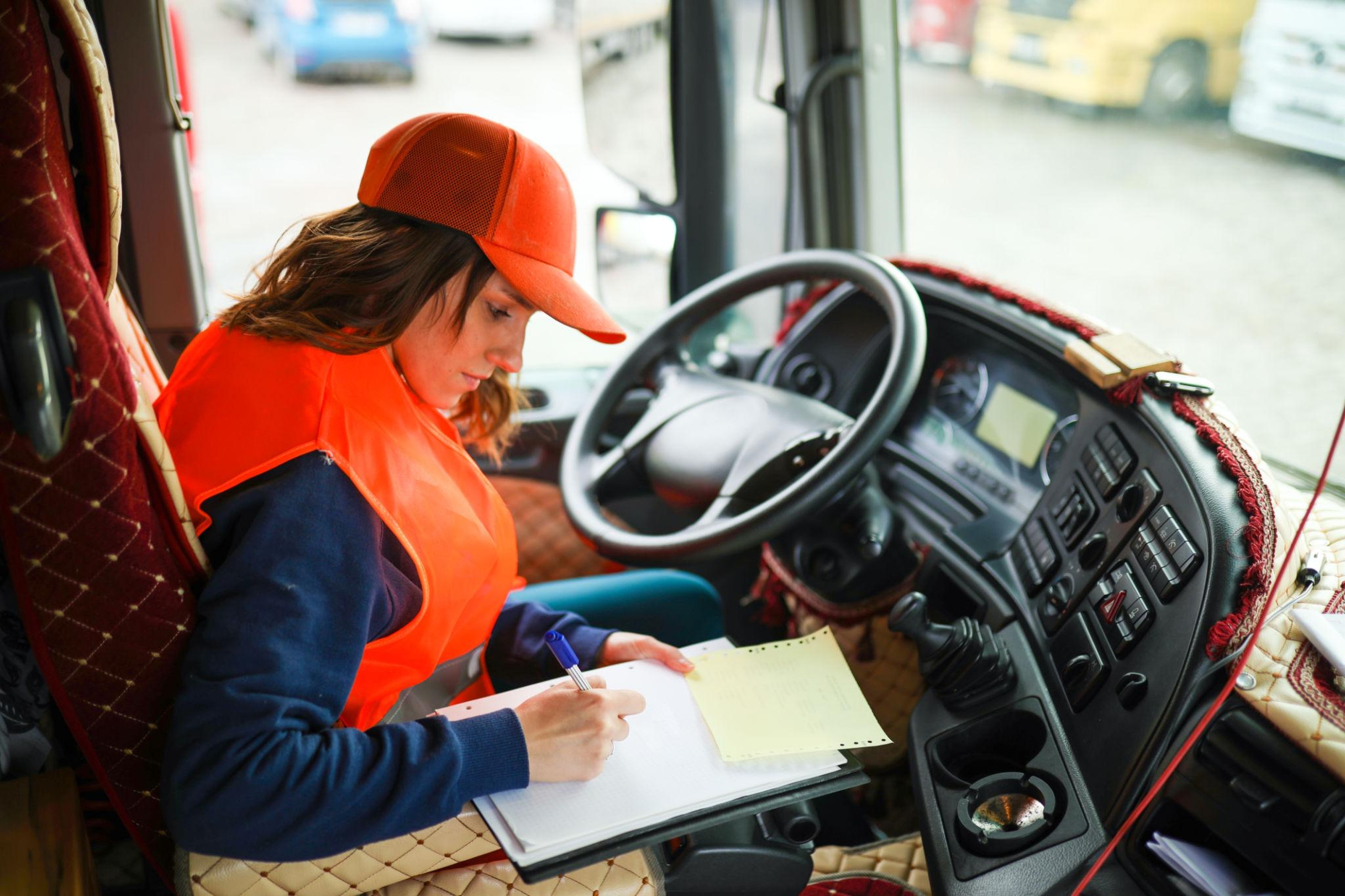 Conductora en la cabina de un camión rellenando a mano el documento de transporte en un cuaderno