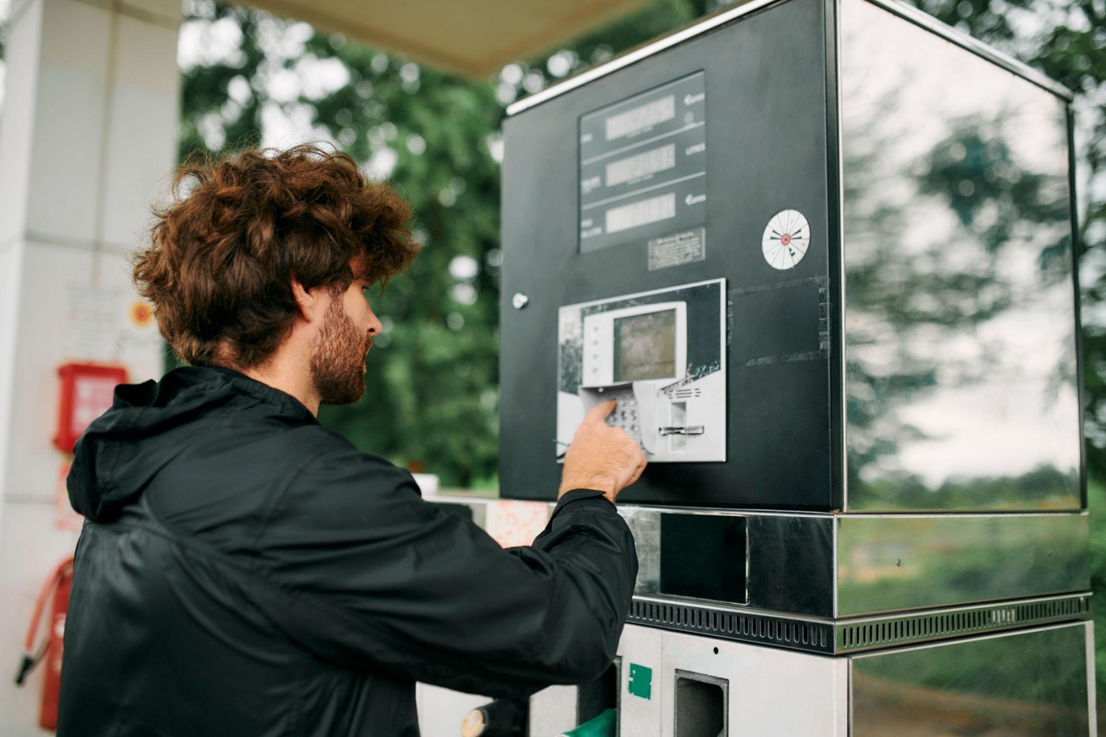 Hombre con chaqueta negra utilizando la pantalla táctil de una gasolinera mientras reposta su camión, imagen ilustrativa sobre la evolución del precio del gasóleo en España.