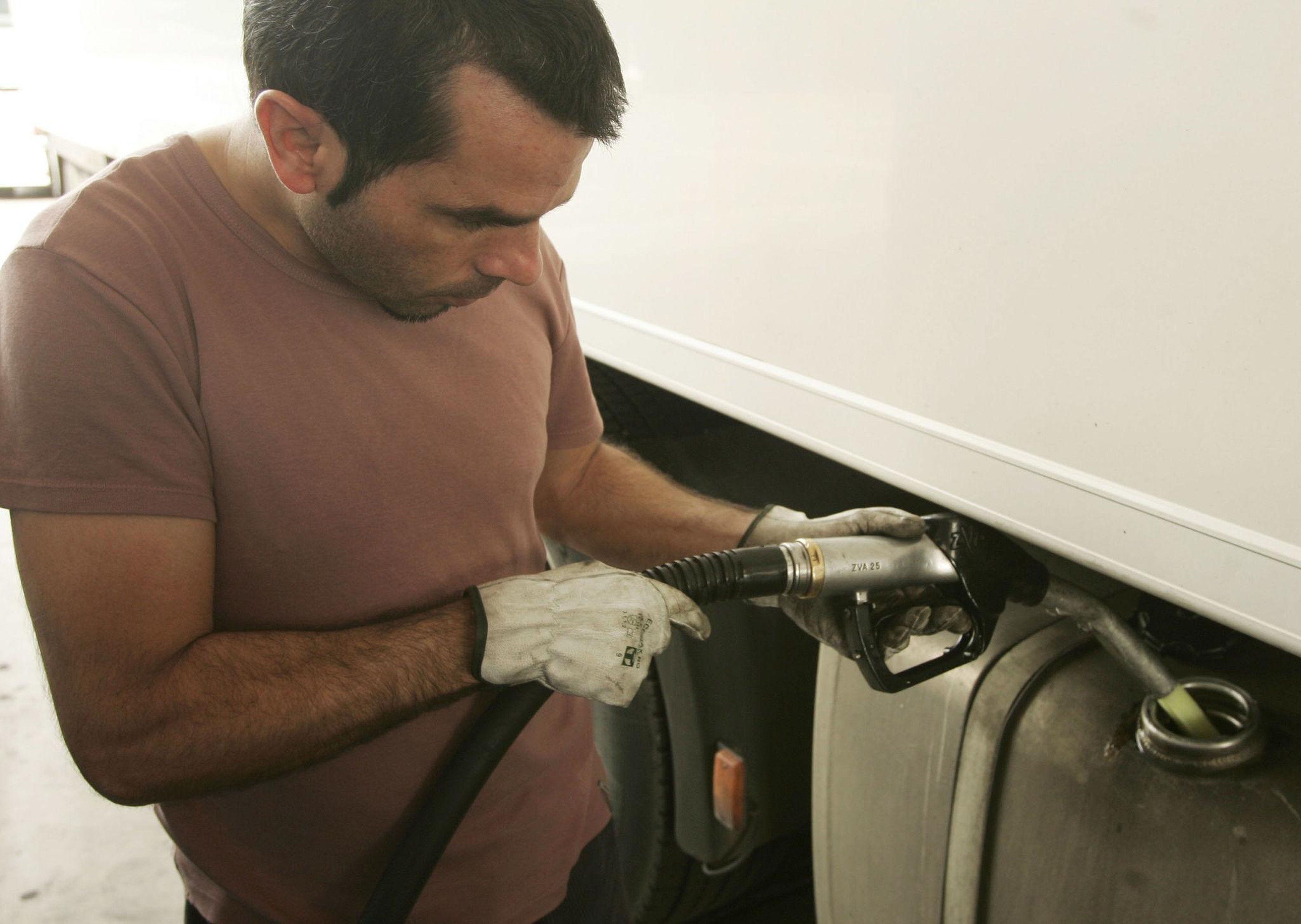 Persona repostando un camión blanco con una manguera de combustible, usando guantes y camiseta marrón en una estación de servicio — escena representativa del uso de gasóleo profesional en transporte por carretera.
