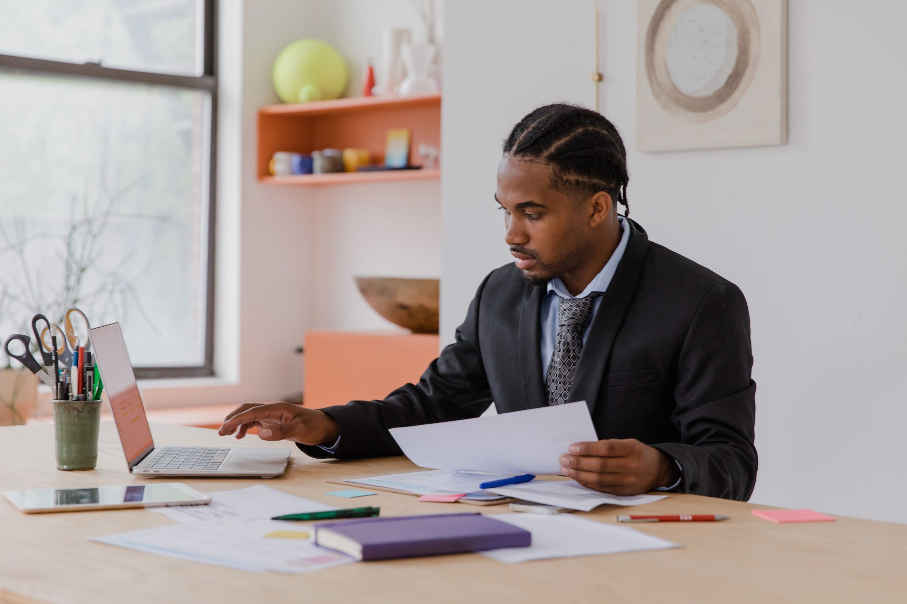 Office professional cross-checking a printed shipping document against his laptop screen while entering order details at his desk