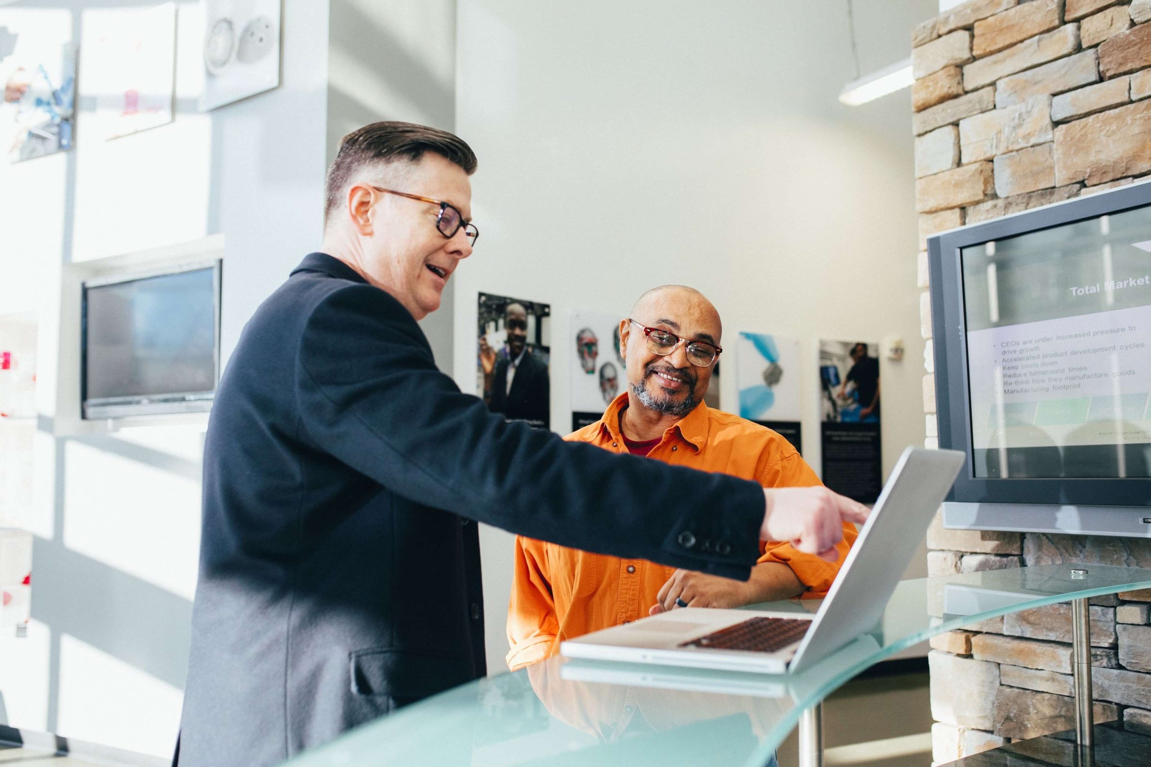 Operations manager walking a colleague through new transportation management software on a laptop in an office