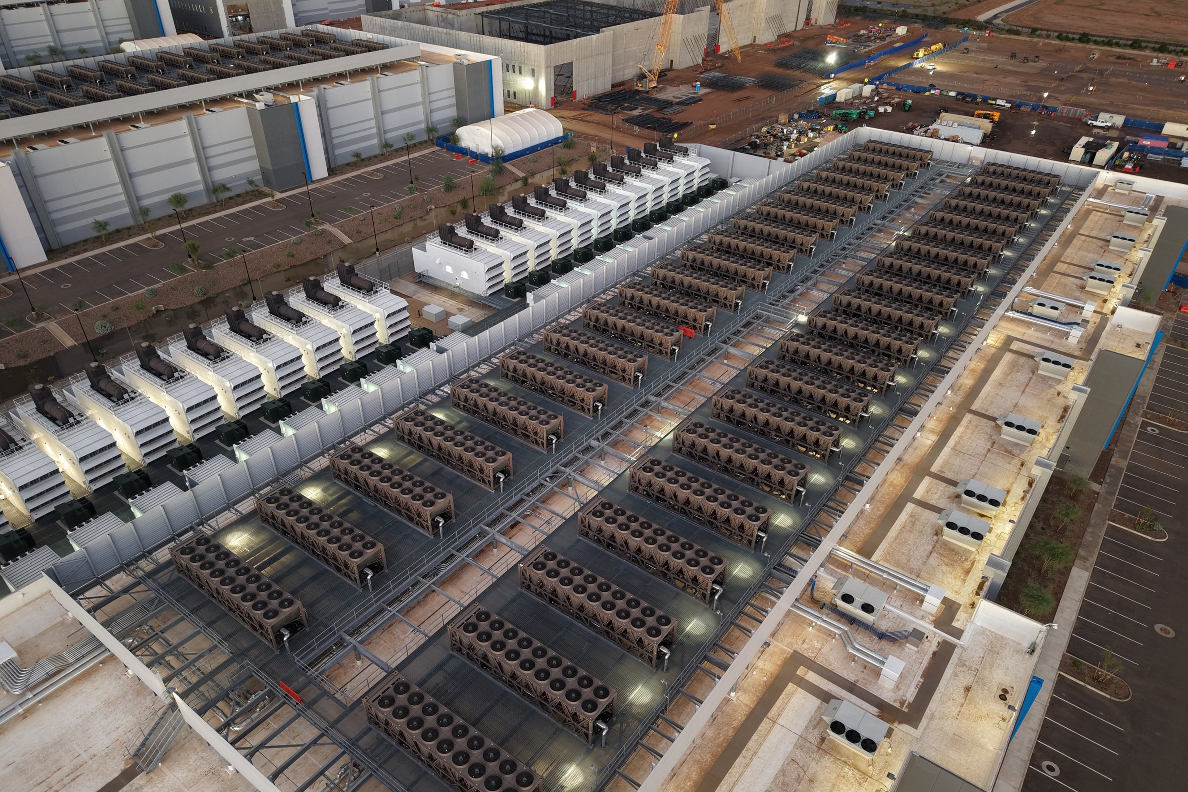 Aerial view of a US data center campus with rooftop cooling units, backup generators and an adjacent construction site with cranes