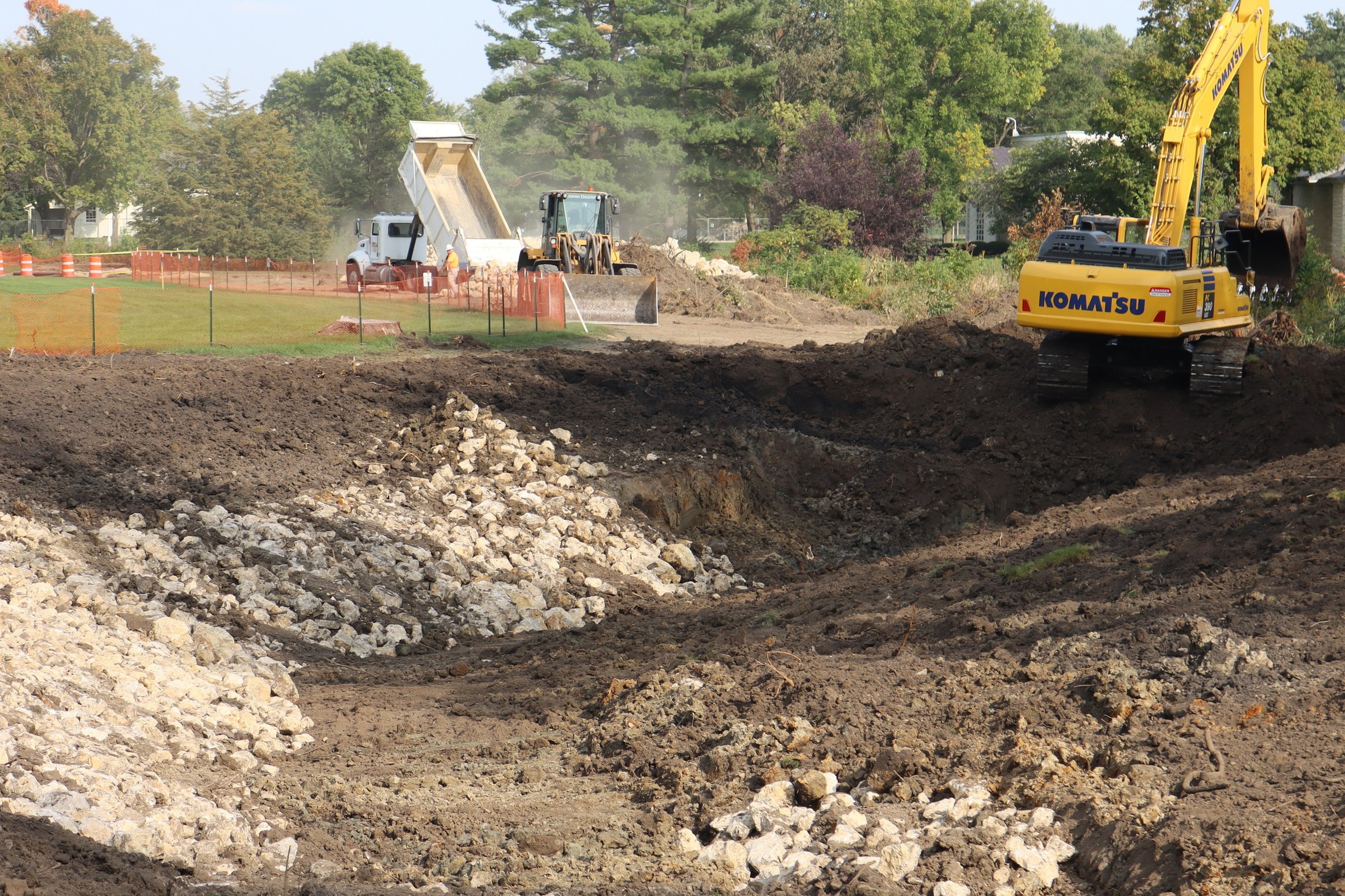 Dump truck tipping a load of rock at a US construction site while an excavator and wheel loader work nearby