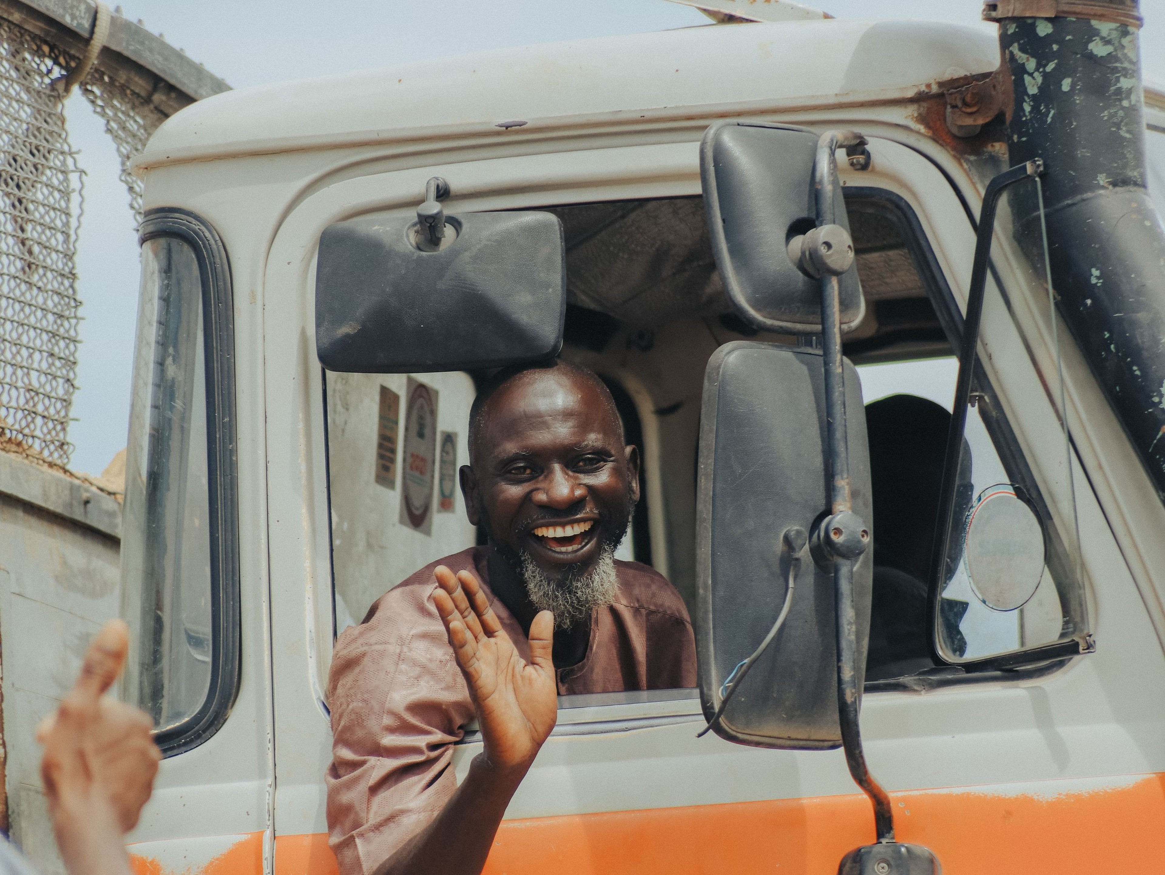 Bearded truck driver smiling and waving from the cab of his semi truck, representing a driver heading back out on the road