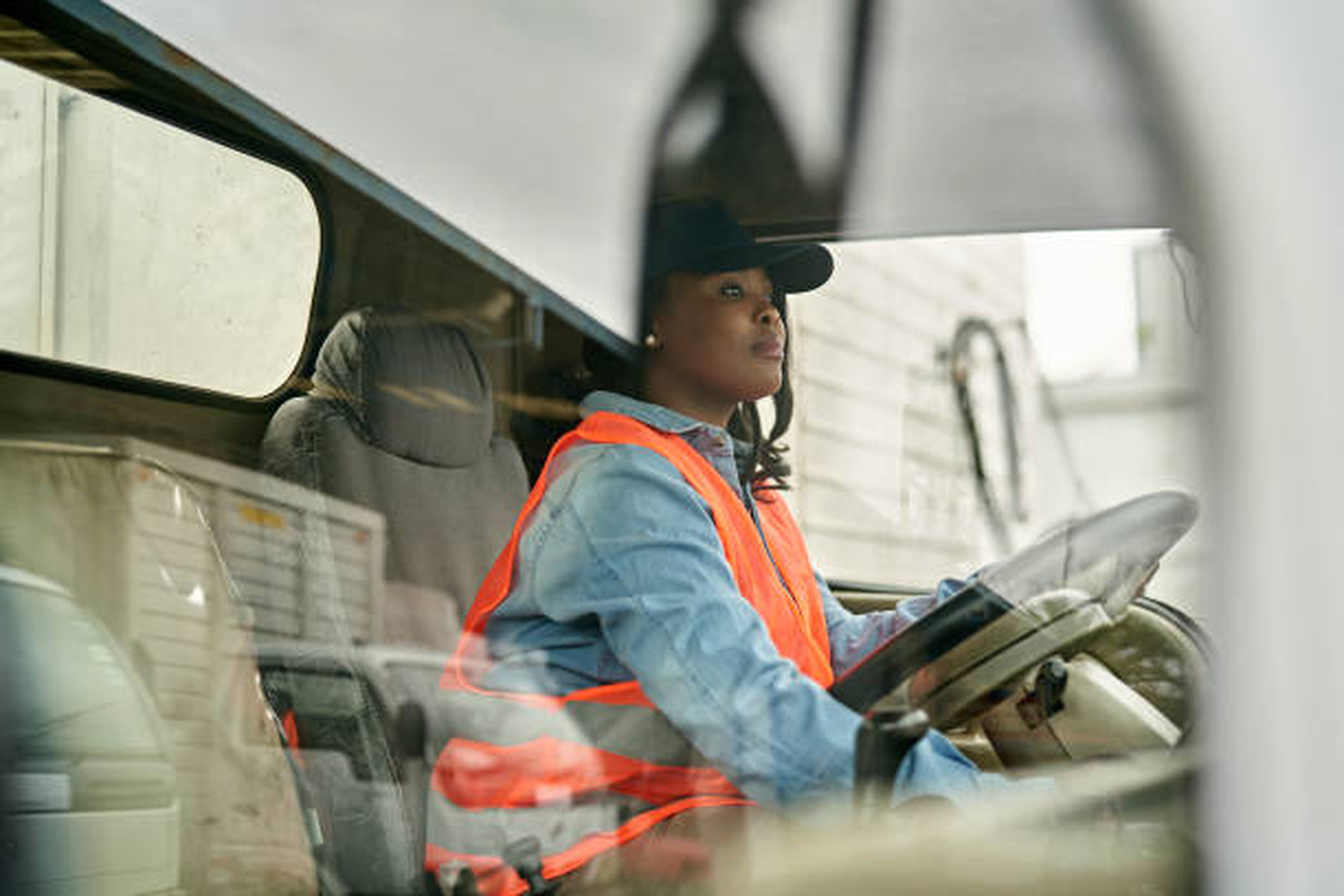 Una persona con chaleco de seguridad y gorra conduce un vehículo, vista desde la ventana exterior, mientras el sistema de GPS telemático supervisa el trayecto.