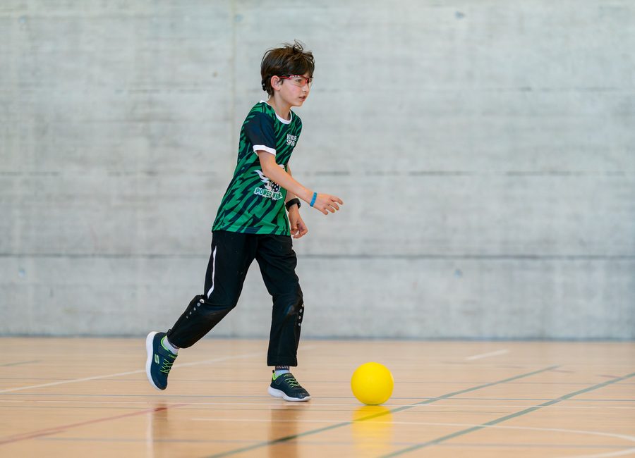 Kind beim Spiel mit einem gelben Ball in der Sporthalle