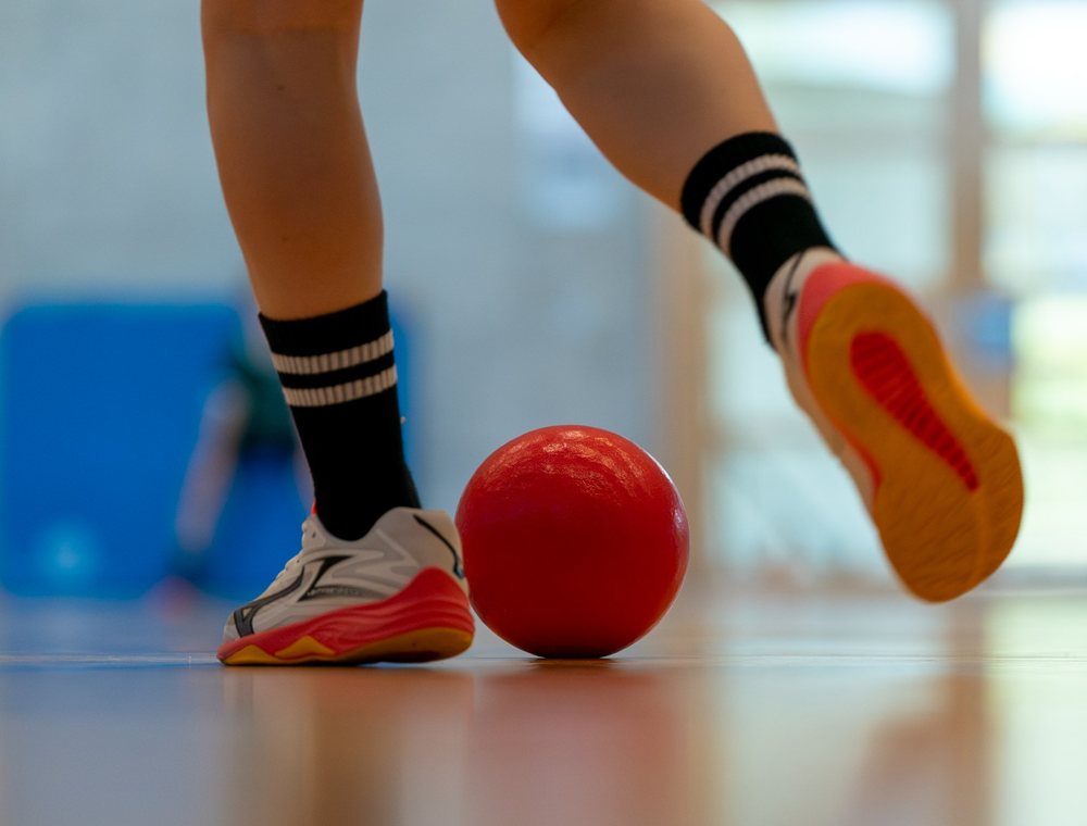 Kinderfüsse und roter Ball in der Sporthalle
