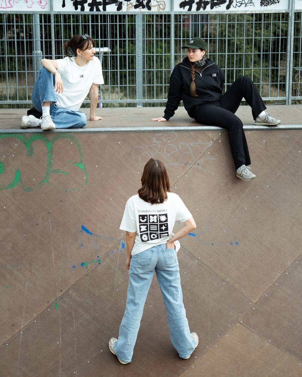 Drei Personen in Franz Johann Shirts, Hoodie und Cap im Skatepark