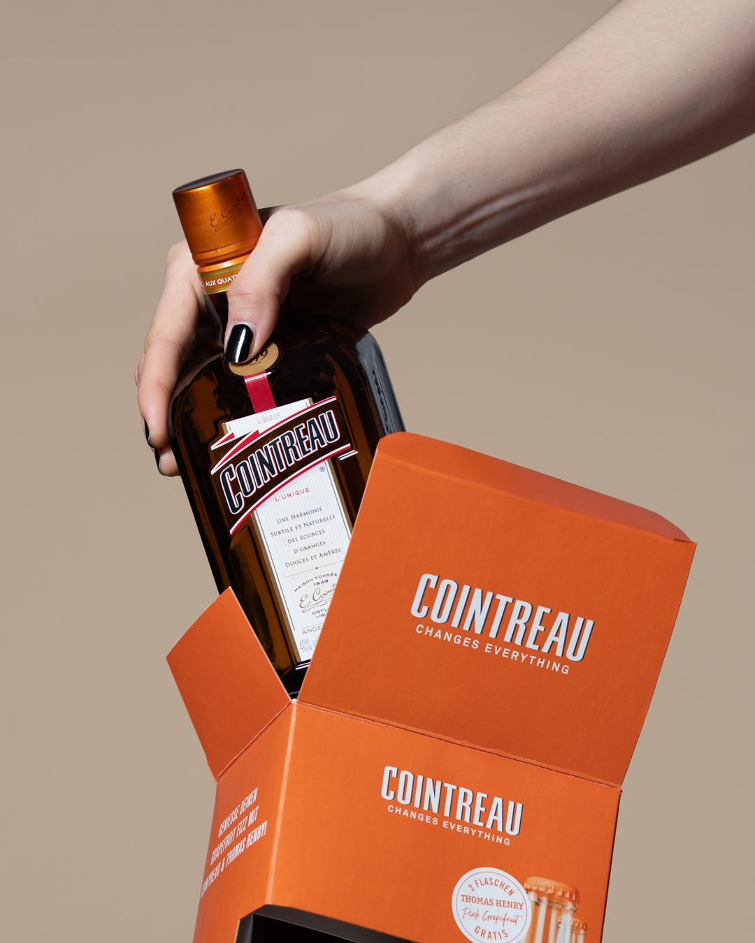 Hände heben eine Cointreau-Flasche aus einer orangen Geschenkverpackung