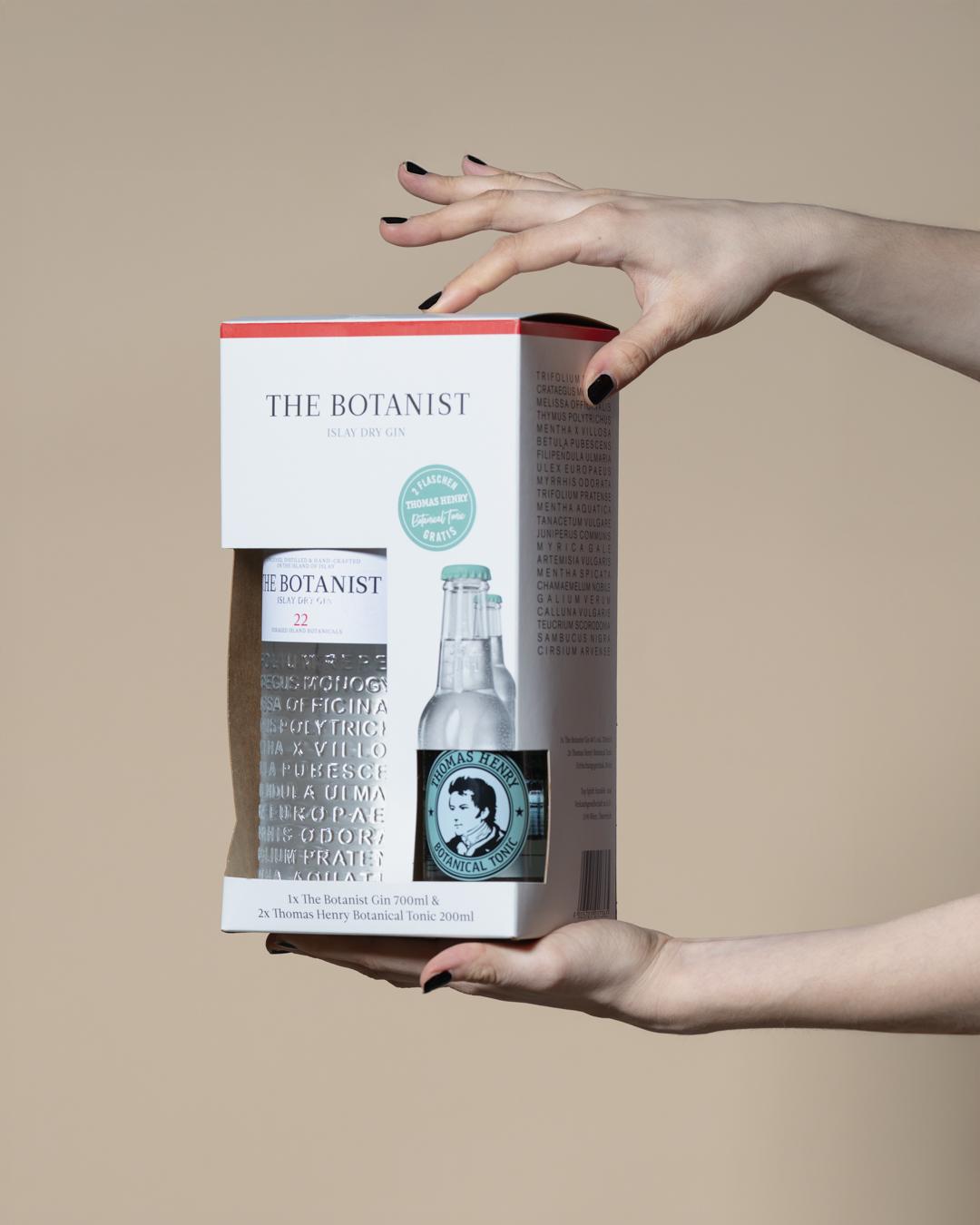 Hände öffnen die Faltschachtel einer The-Botanist-Gin-Flasche