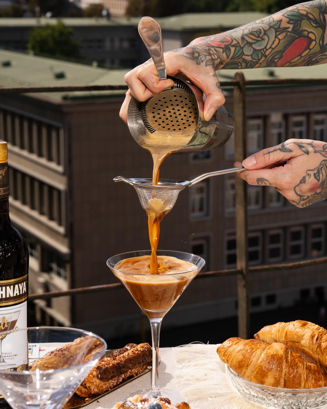 Hand seiht einen Cocktail durch ein Barsieb in ein Glas