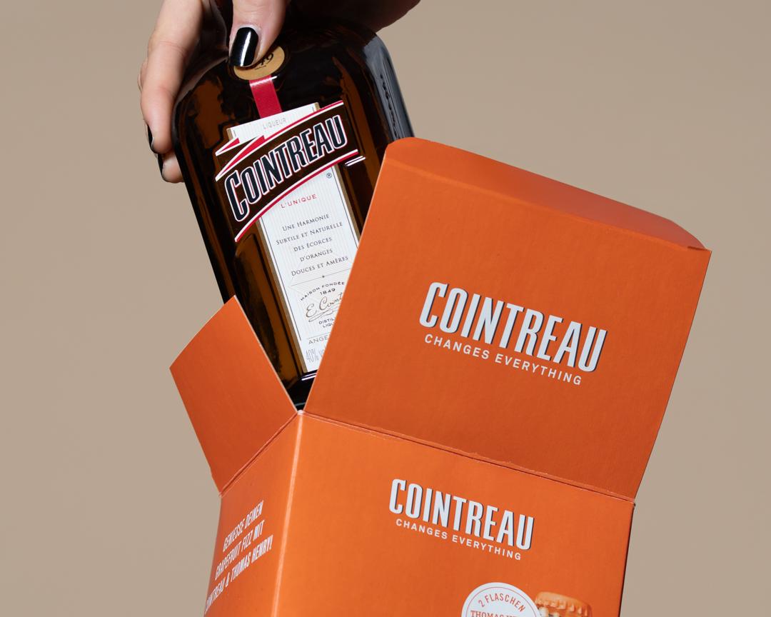 Hand zieht eine Cointreau-Flasche aus der orangen Geschenkbox