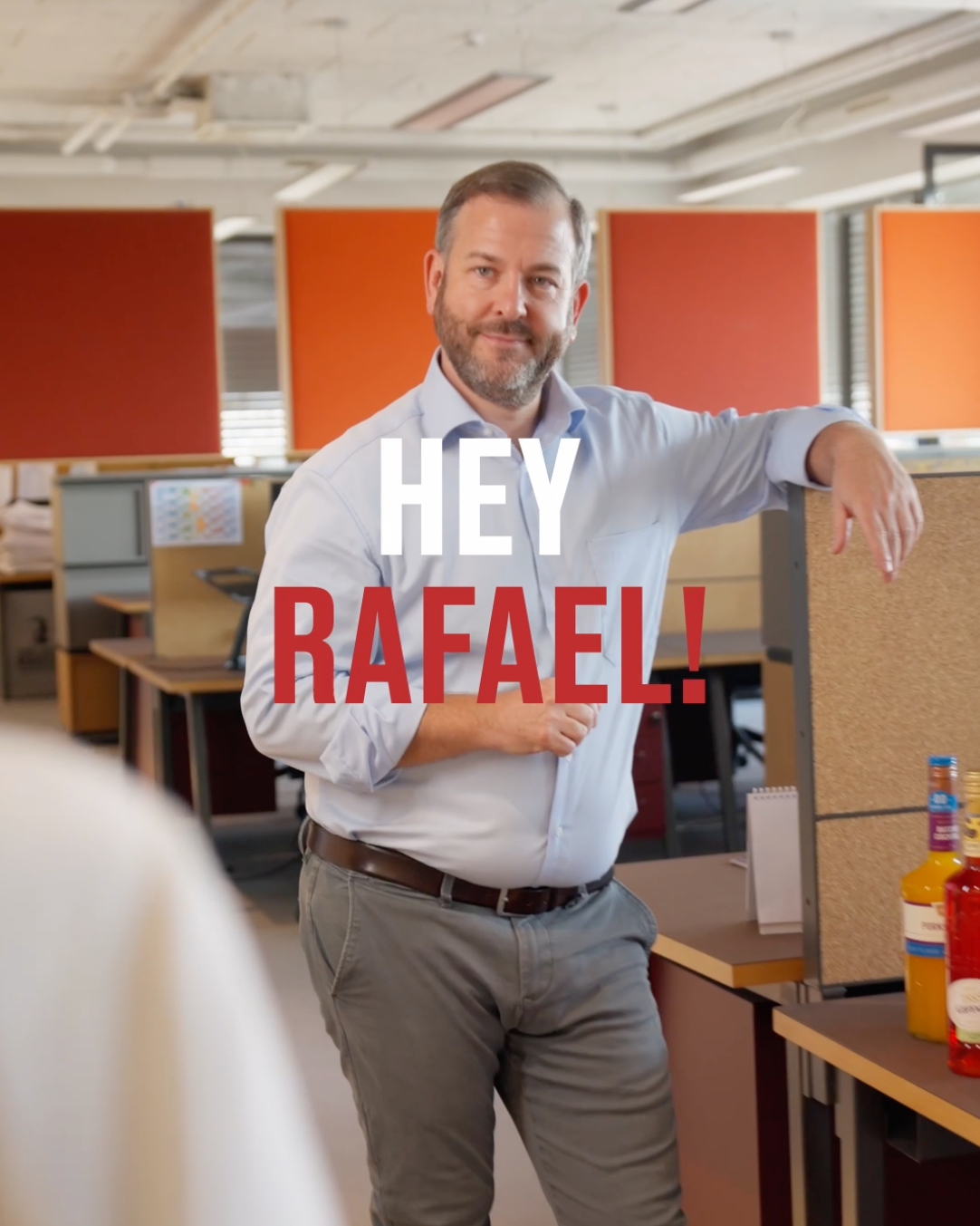 Mann im Büro lehnt an einer Trennwand, eingeblendet „Hey Rafael!“