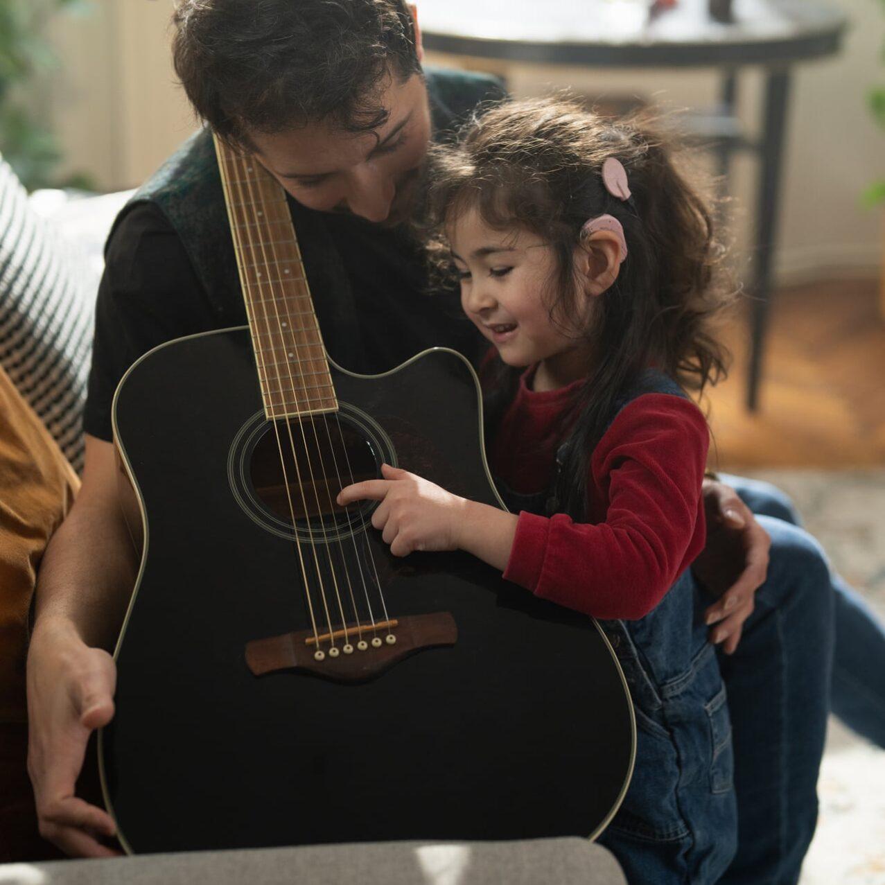 Kleine Ayla mit ihrem Vater und einer Gitarre auf dem Sofa
