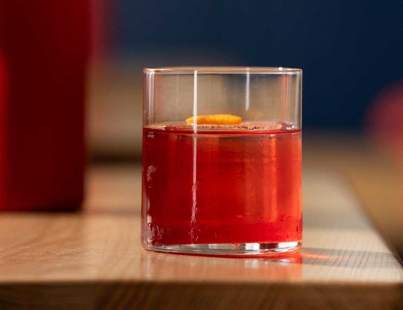 Roter Drink im Glas auf einem Holztisch, davor eine rote Tischleuchte