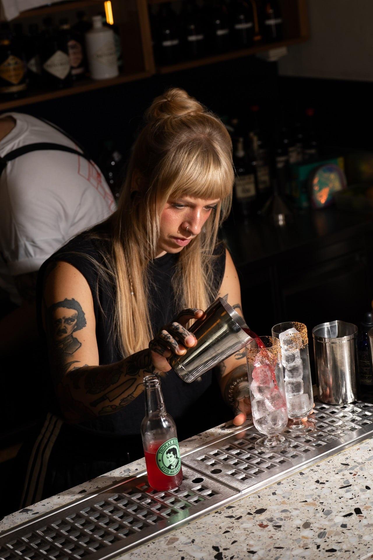 Barkeeperin mit Pony schüttelt am Tresen einen Drink im Shaker
