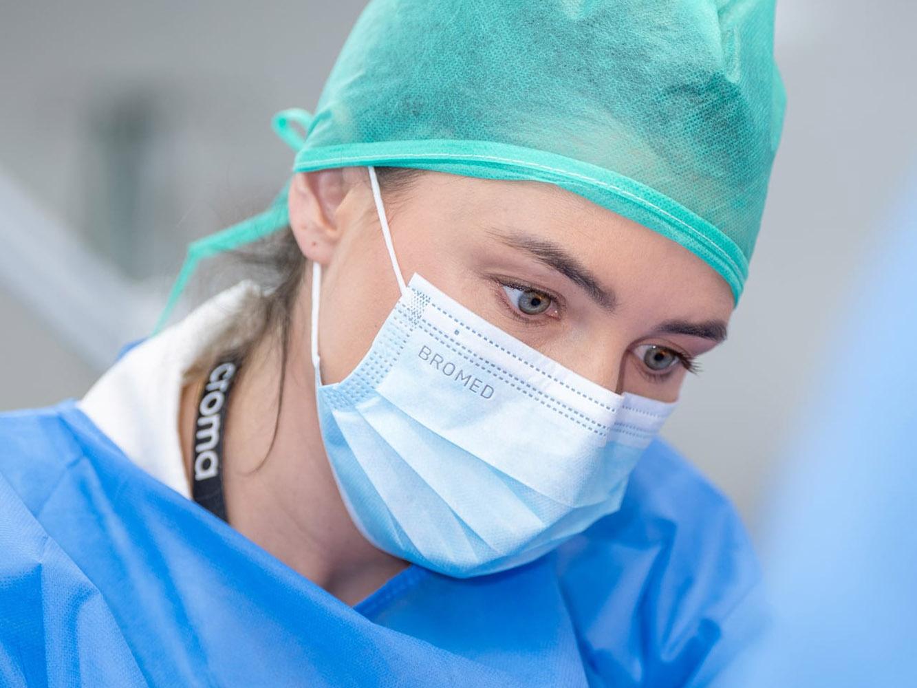 Frau in OP-Kleidung mit Haube, Maske und Handschuhen bei einem praktischen Kurs