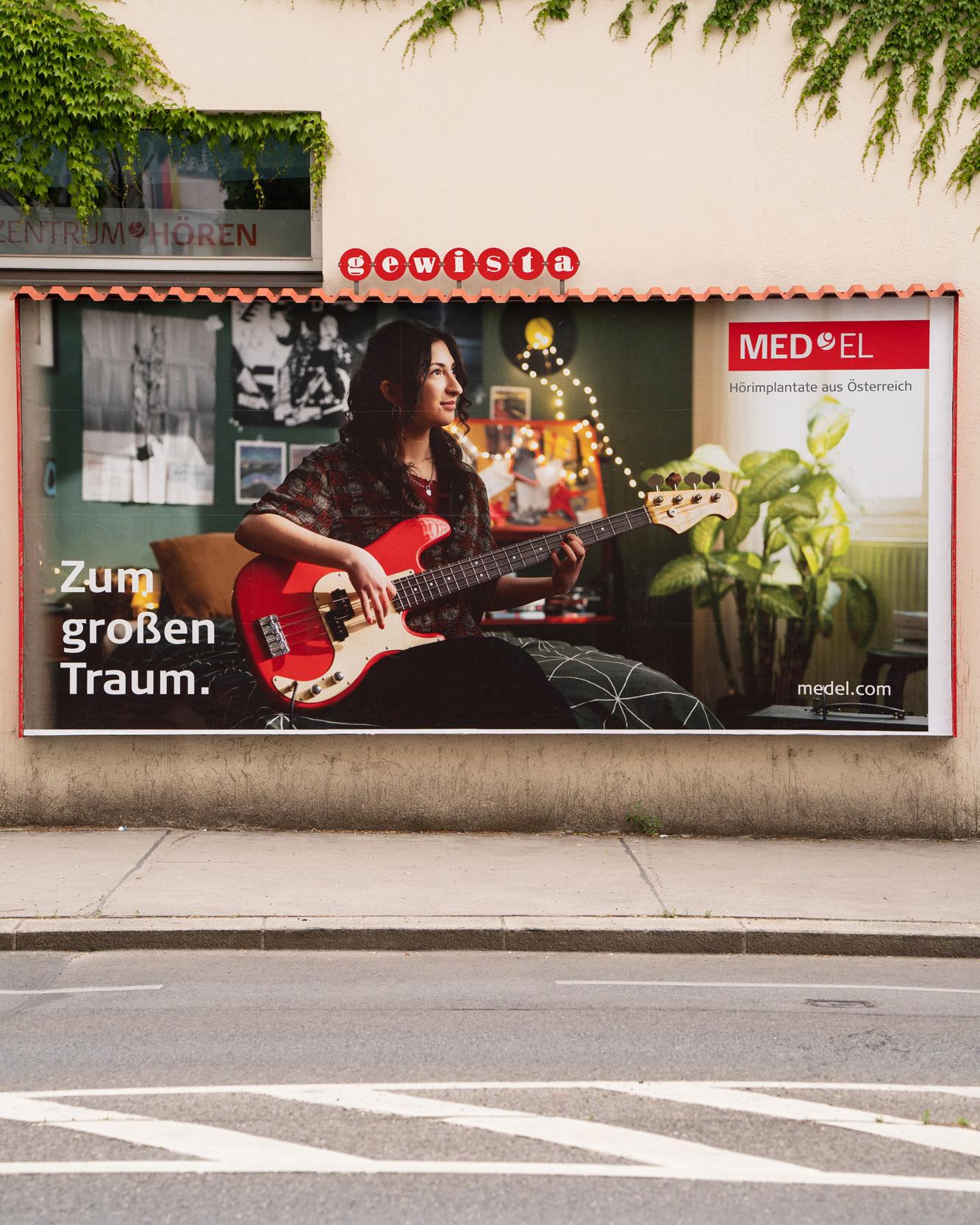 MED-EL-Plakat „Zum großen Traum“ mit Gitarristin an einer Hauswand