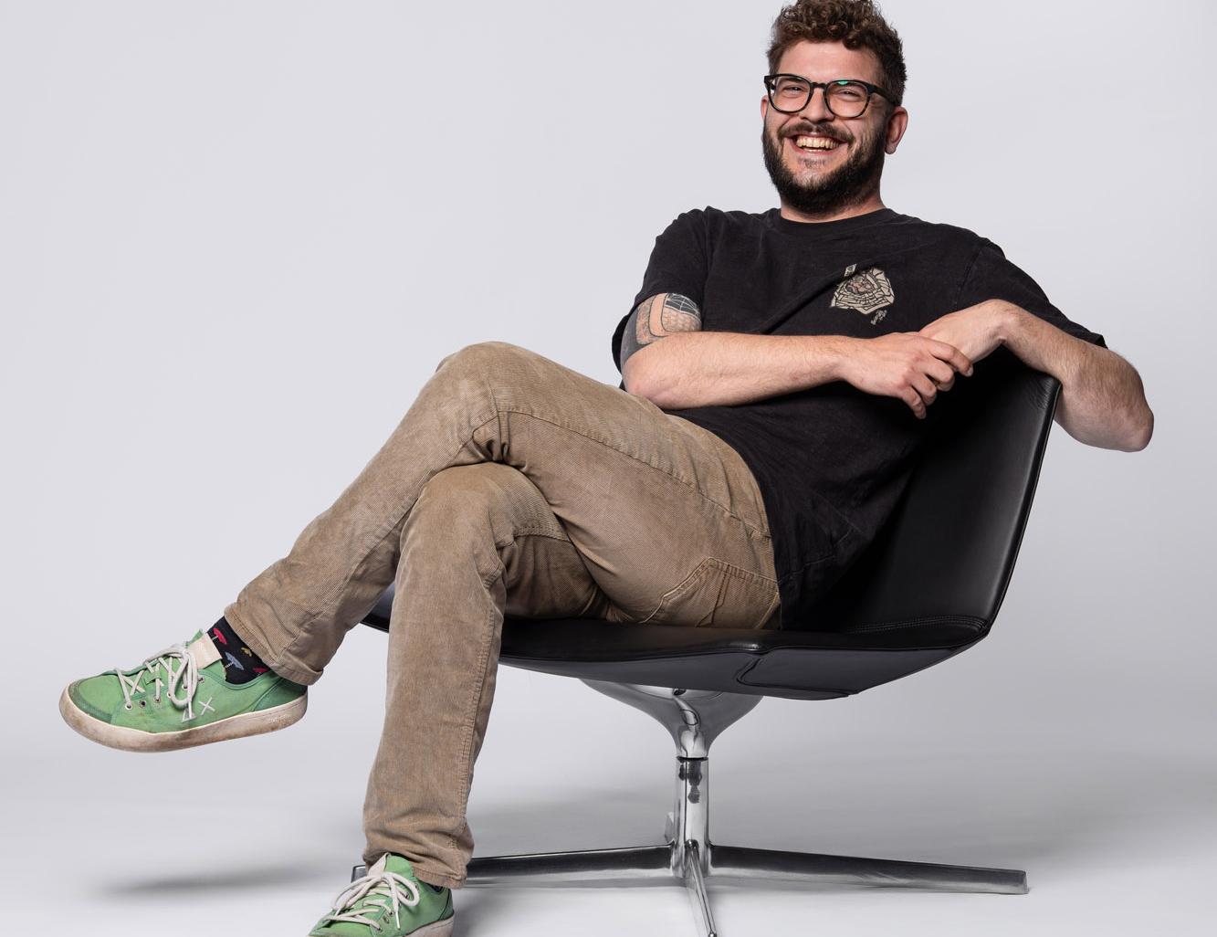Mann im schwarzen Shirt sitzt entspannt seitlich auf einem Stuhl