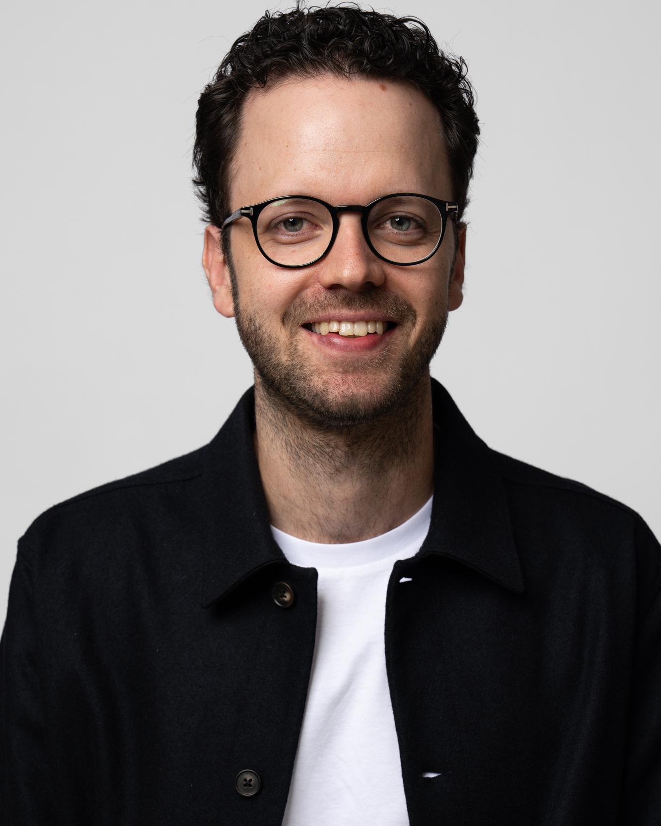 Portrait von Philipp Hicker im schwarzen Hemd vor hellem Hintergrund
