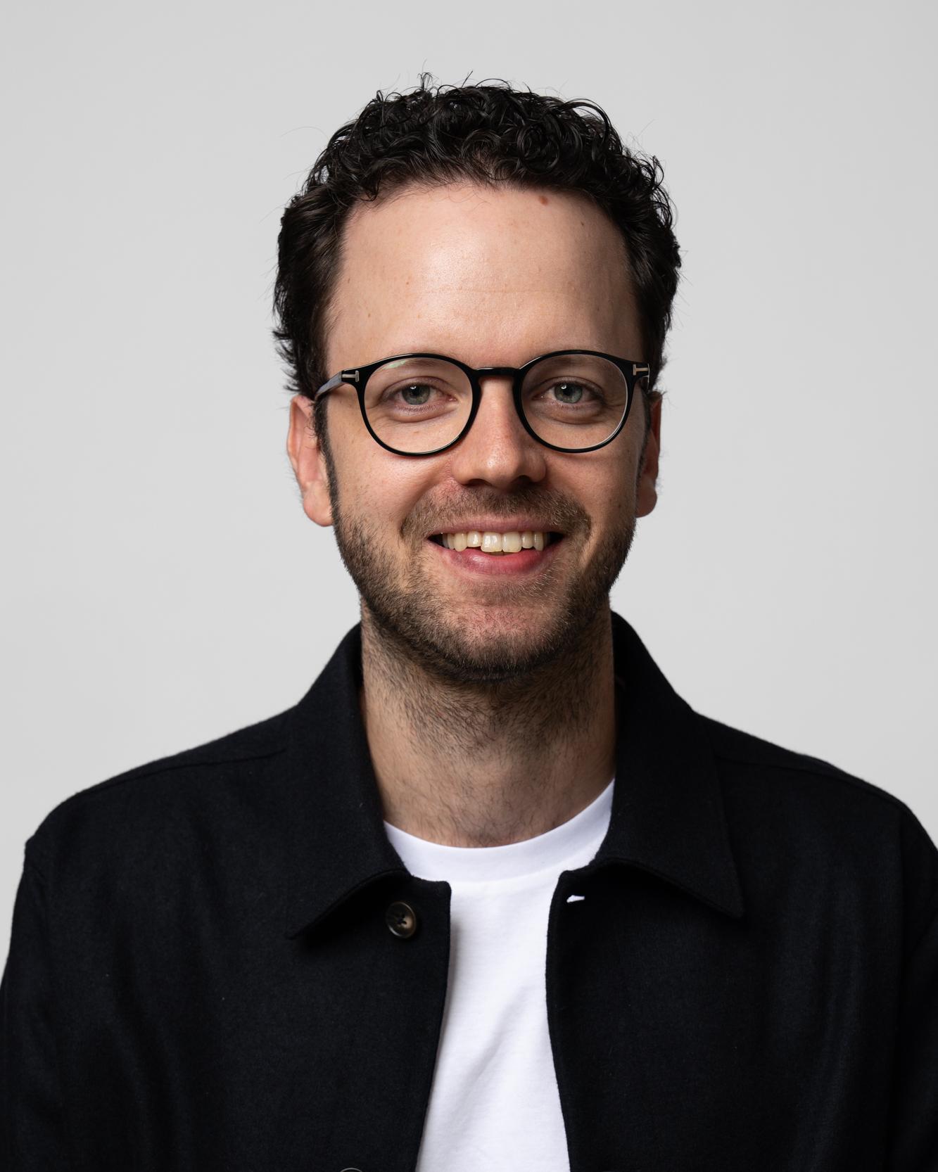 Portrait von Philipp Hicker im schwarzen Hemd vor hellem Hintergrund