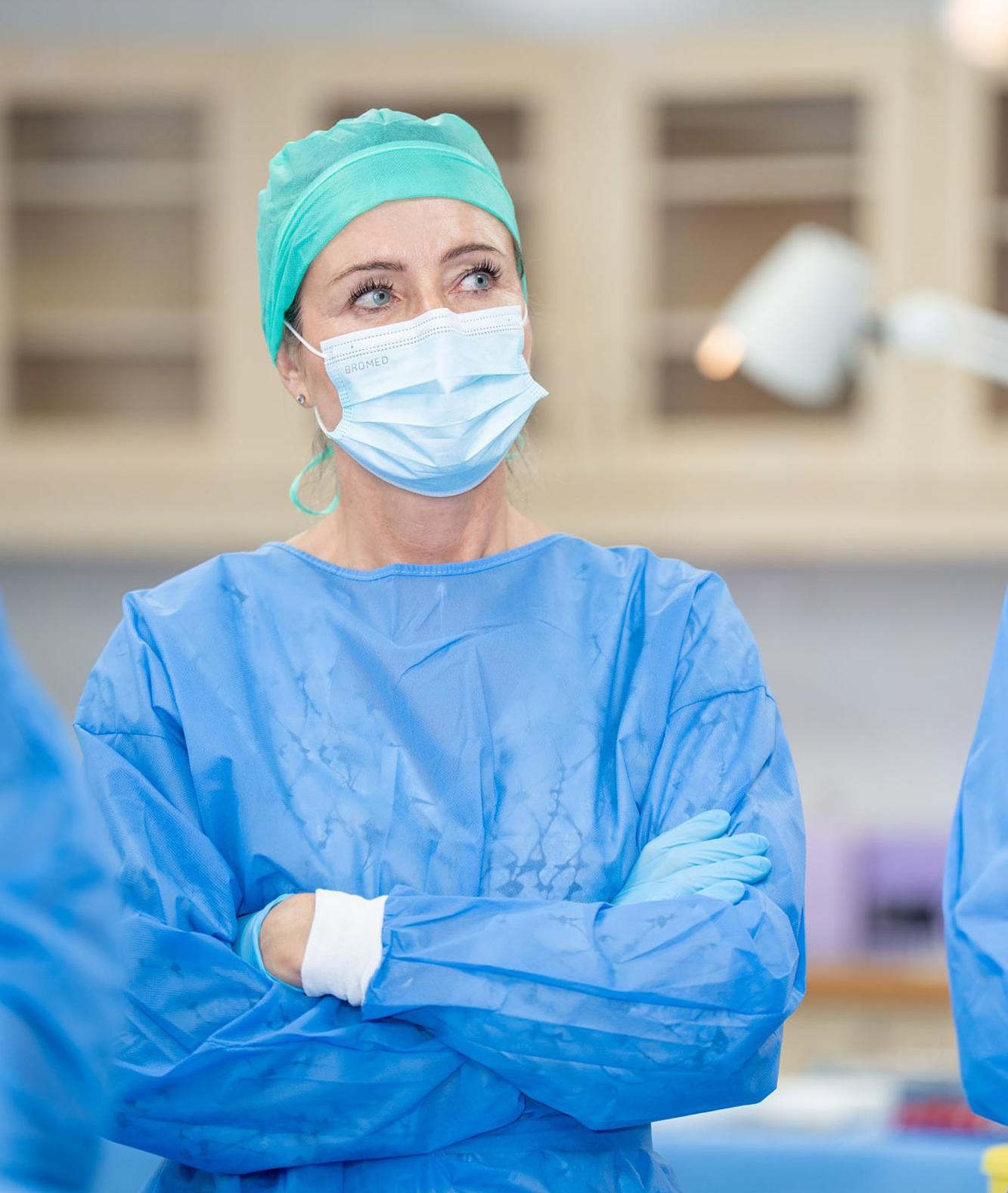 Ärztin mit Maske und blauem OP-Kittel bei der Arbeit
