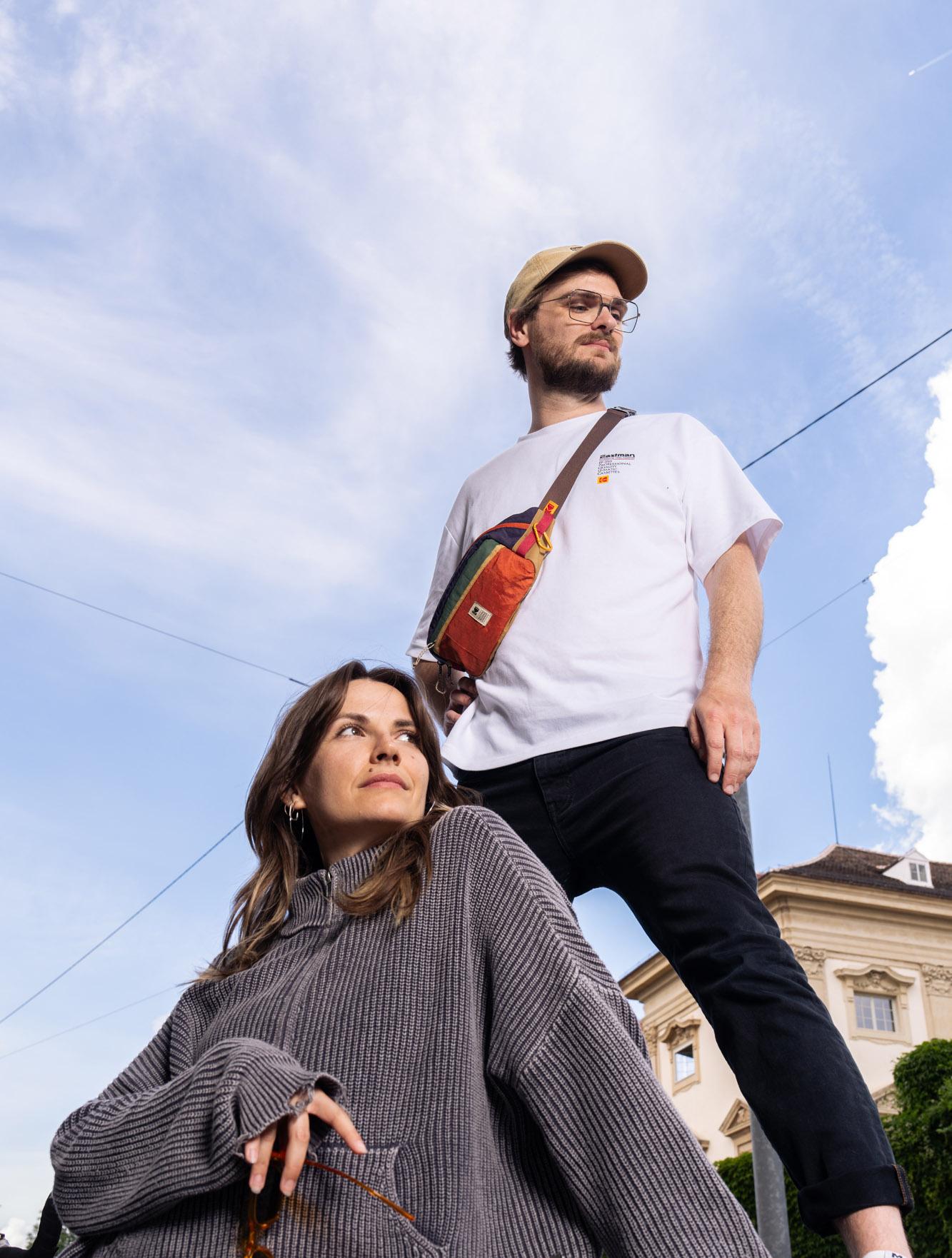 Zwei Personen vor blauem Himmel, eine mit Umhängetasche