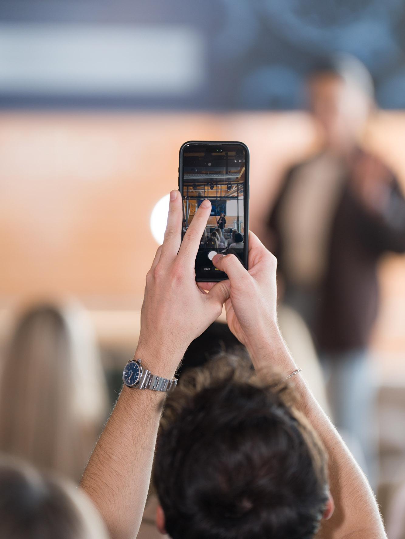 Zuhörer filmt mit dem Smartphone einen Vortrag auf der Bühne