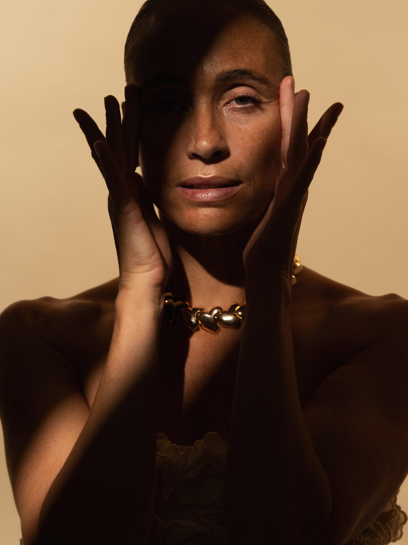 Frau rahmt ihr Gesicht mit beiden Händen, Lichtstreifen über den Augen, goldene Kette