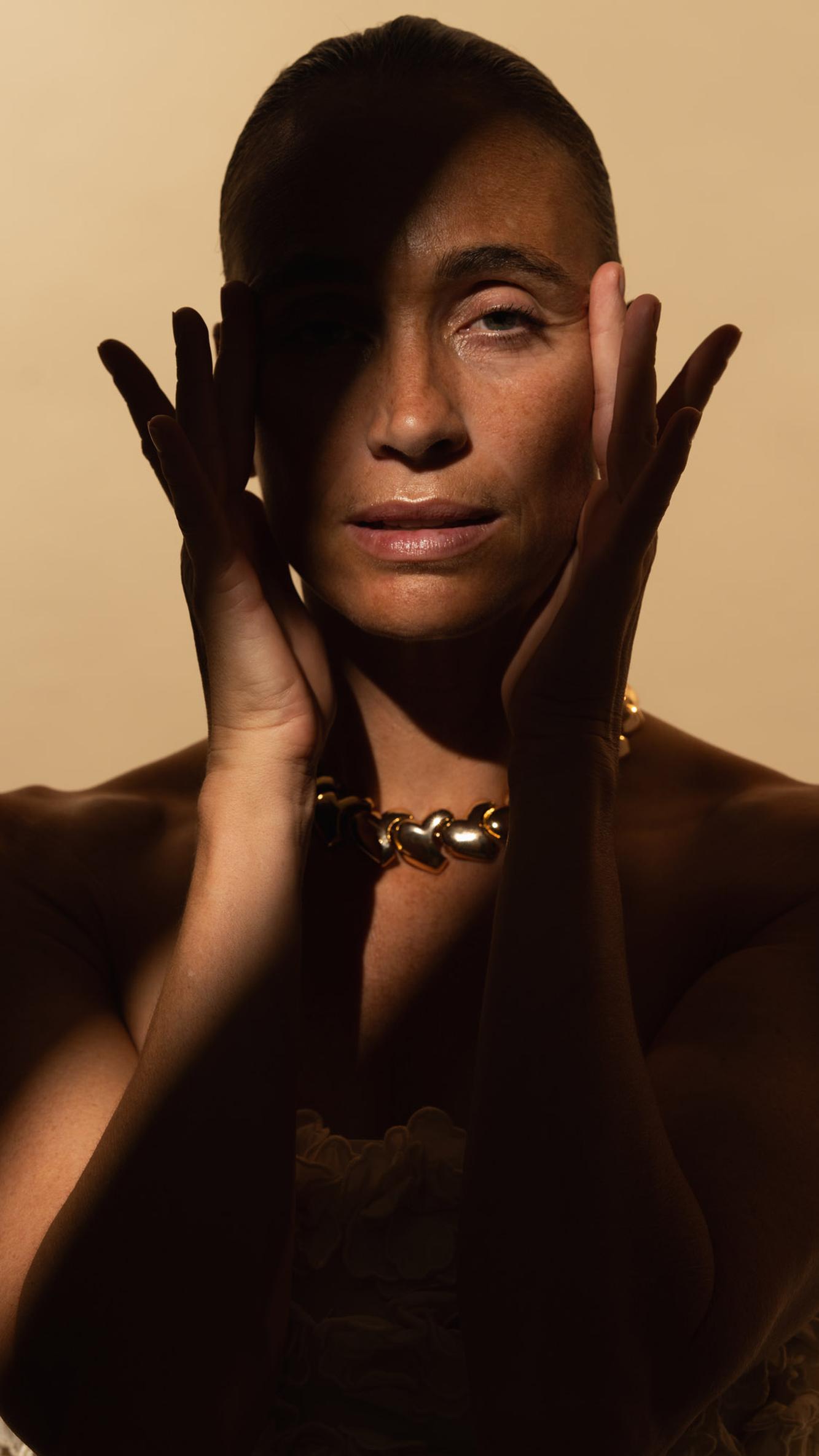 Frau rahmt ihr Gesicht mit beiden Händen, Lichtstreifen über den Augen, goldene Kette