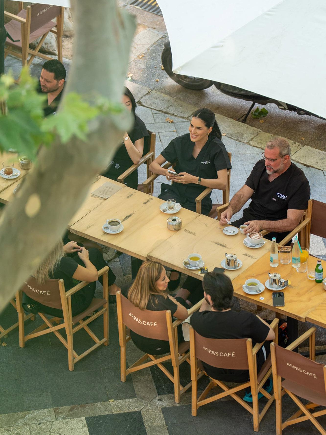 Gruppe in schwarzer Teamkleidung beim Kaffee an einem Tisch im Freien, von oben fotografiert