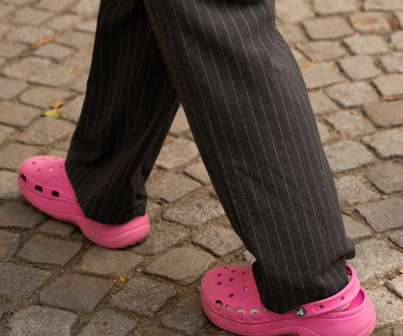 Zwei Personen in pinken Clogs und Nadelstreifenhose auf Kopfsteinpflaster