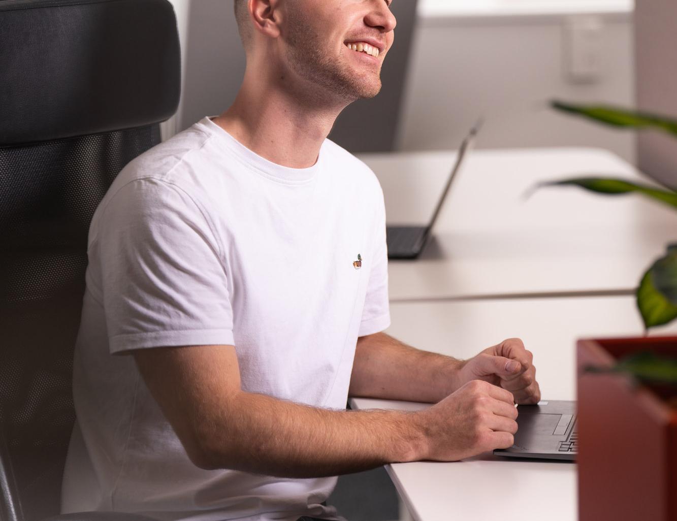 Mann im weißen T-Shirt arbeitet am Laptop in einem Büro