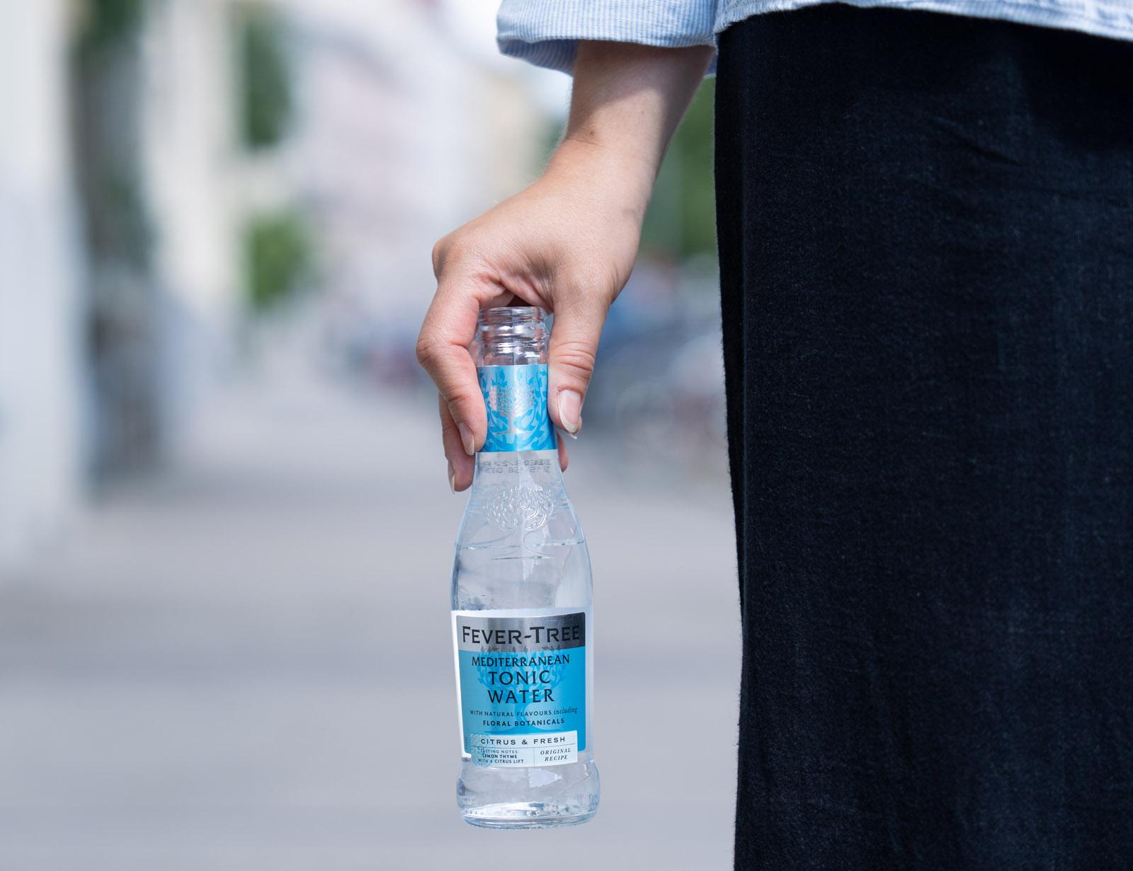 Hand hält eine Fever-Tree-Tonic-Flasche neben einer Jeans