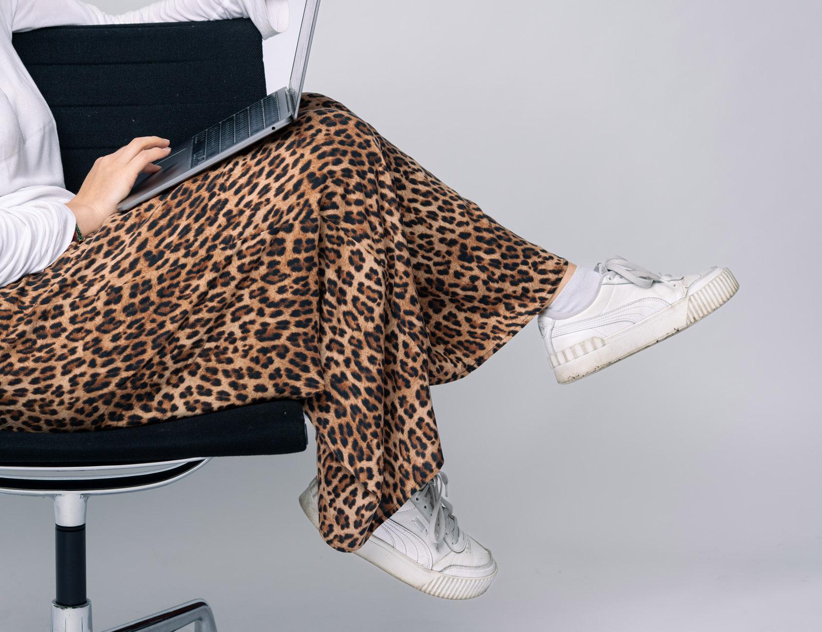 Person mit Leopardenrock und weißen Sneakern sitzt auf einem Bürostuhl