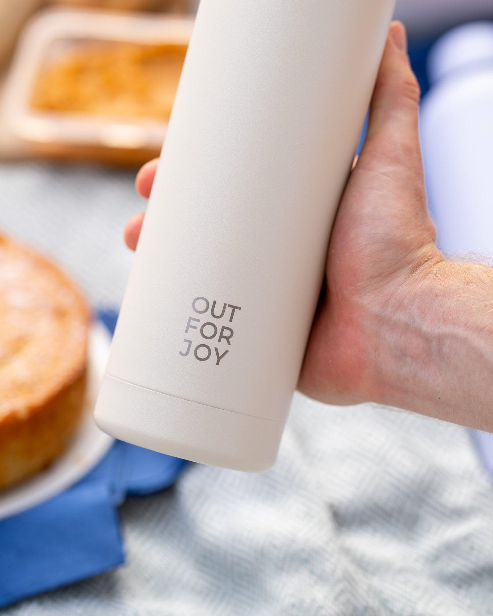 Cremefarbene Out For Joy Trinkflasche mit gelasertem Logo in einer Hand