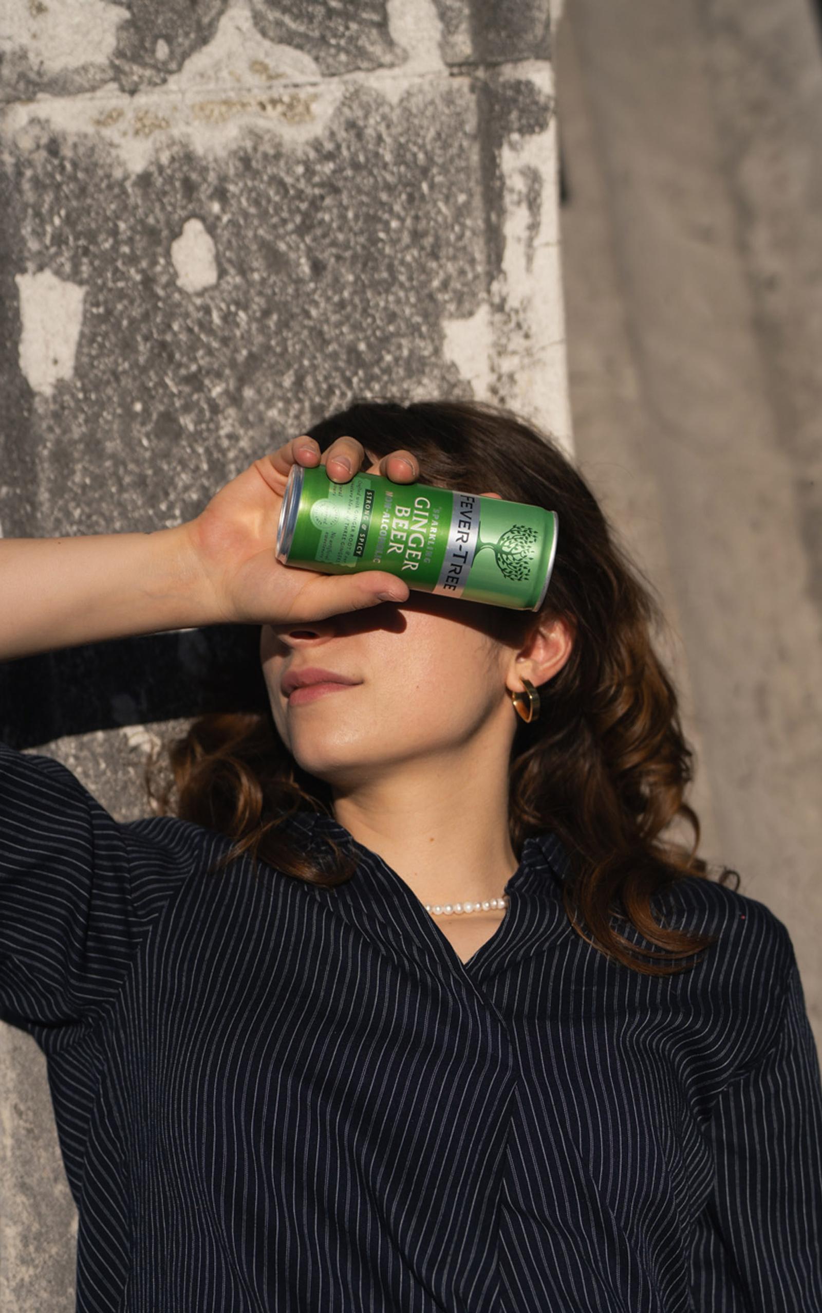 Frau hält sich eine Ginger-Beer-Dose vors Auge