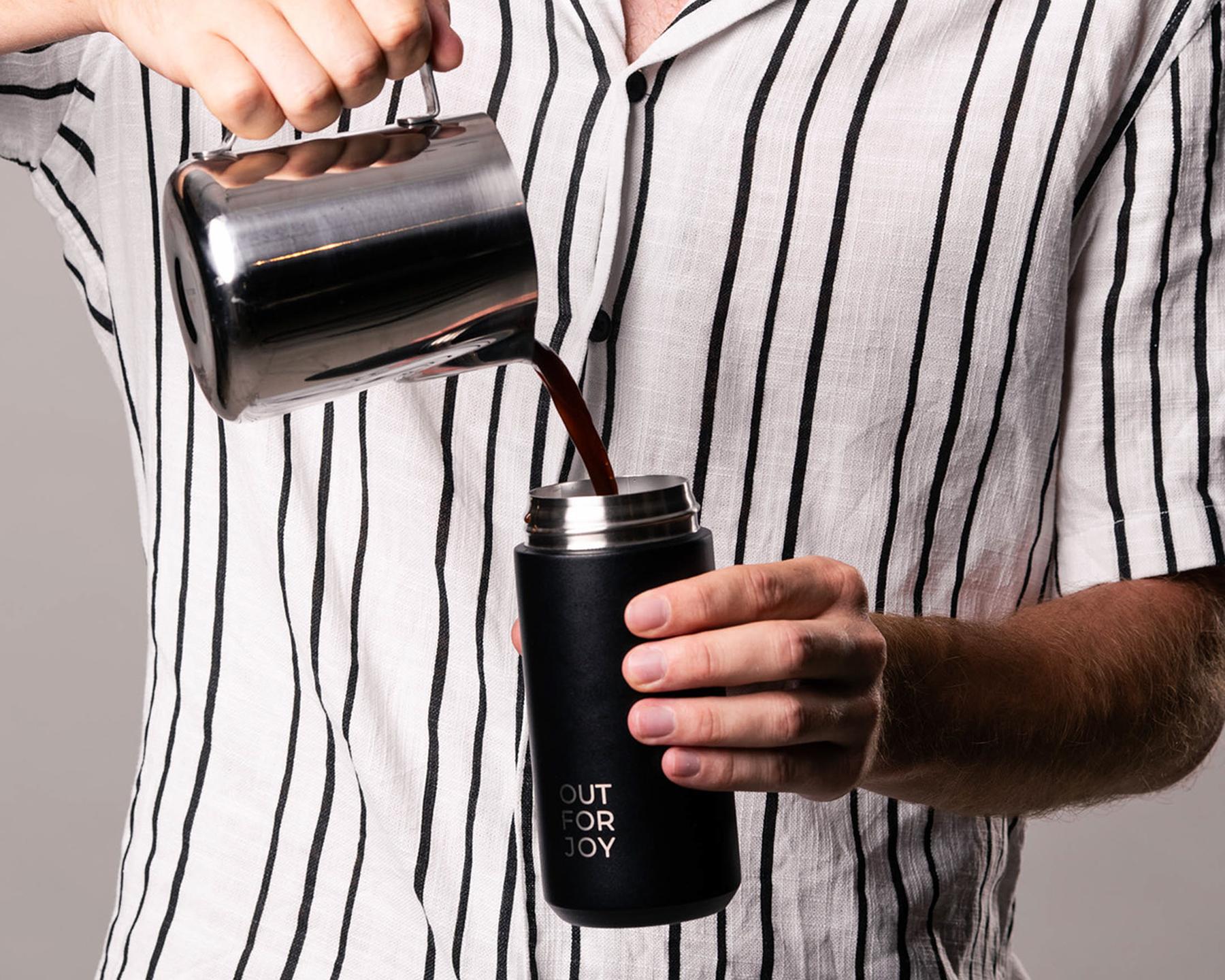 Kaffee wird aus einer Kanne in eine schwarze Thermosflasche gegossen