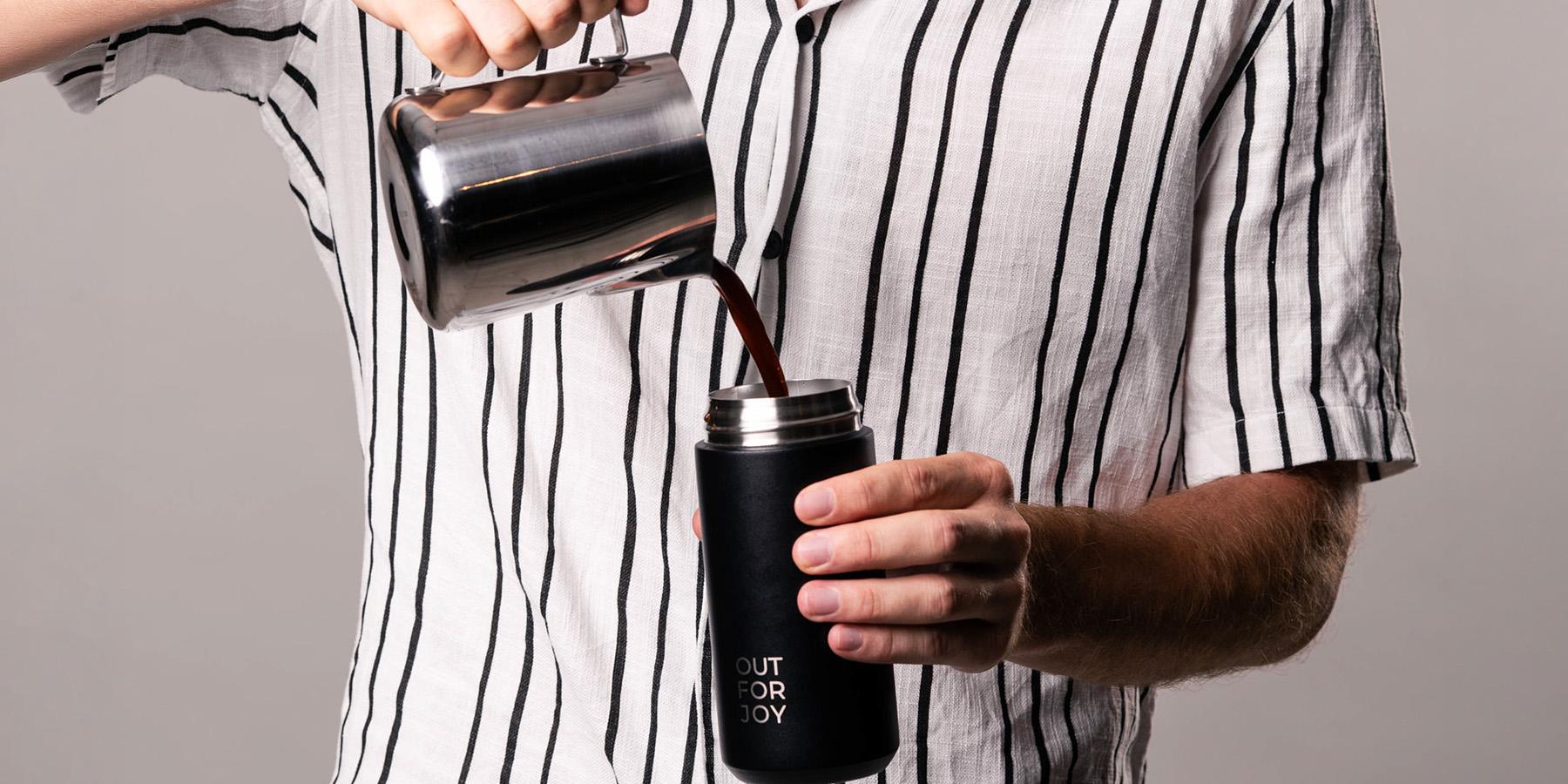 Kaffee wird aus einer Kanne in eine schwarze Thermosflasche gegossen