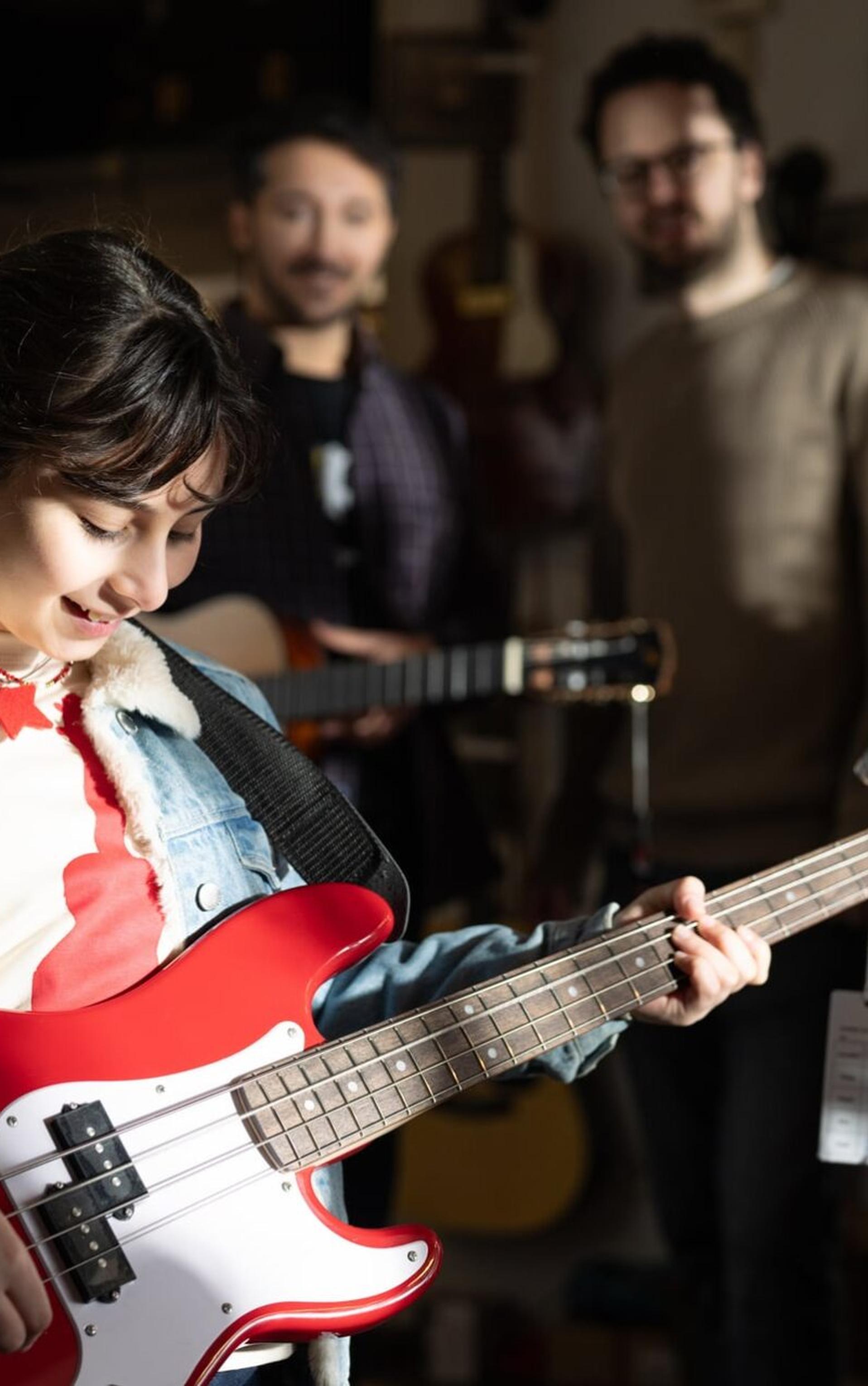 Ayla als Kind spielt in einem Gitarrengeschäft auf einem roten Bass