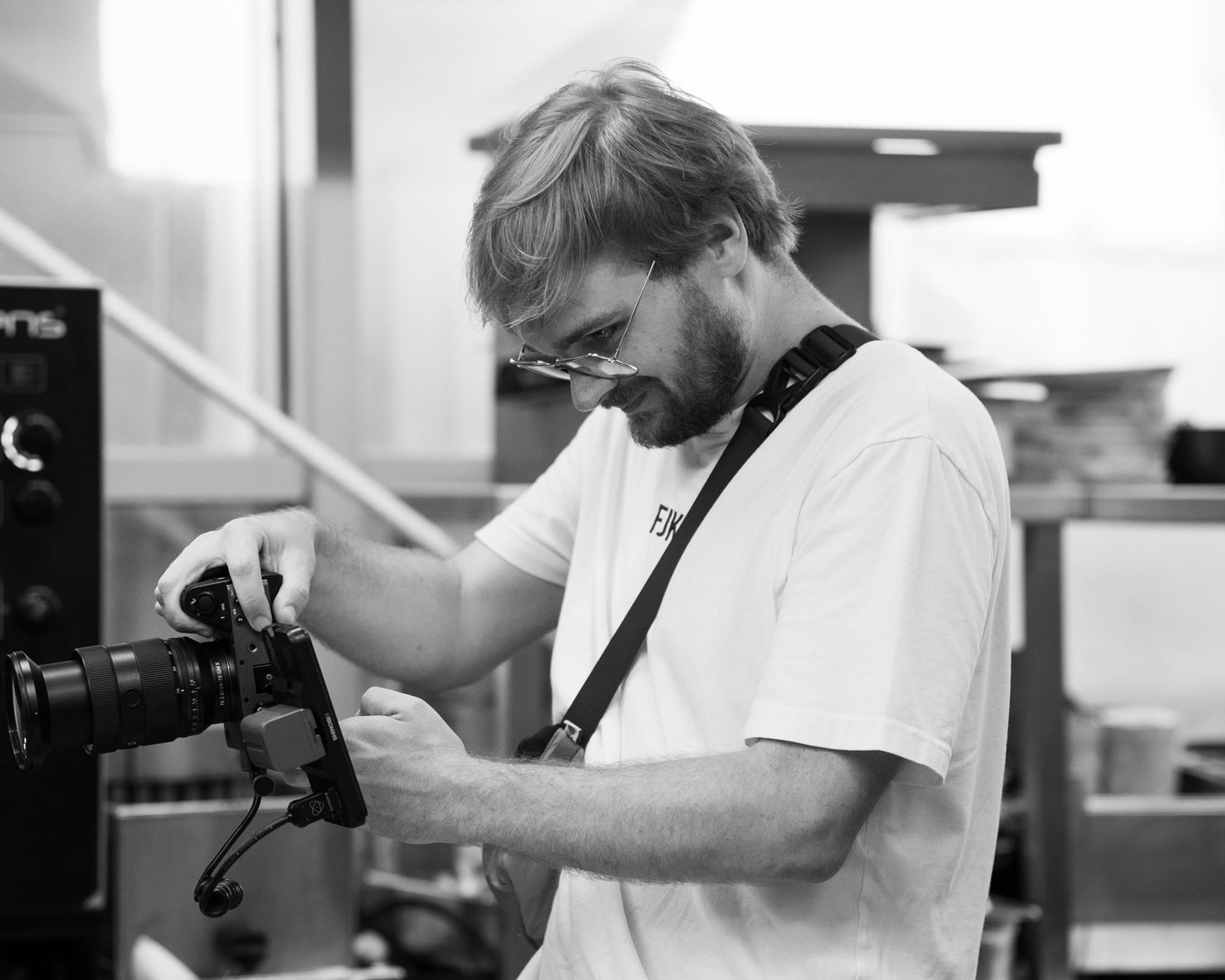 Schwarzweiß: Fotograf mit Kamera in einer Küche